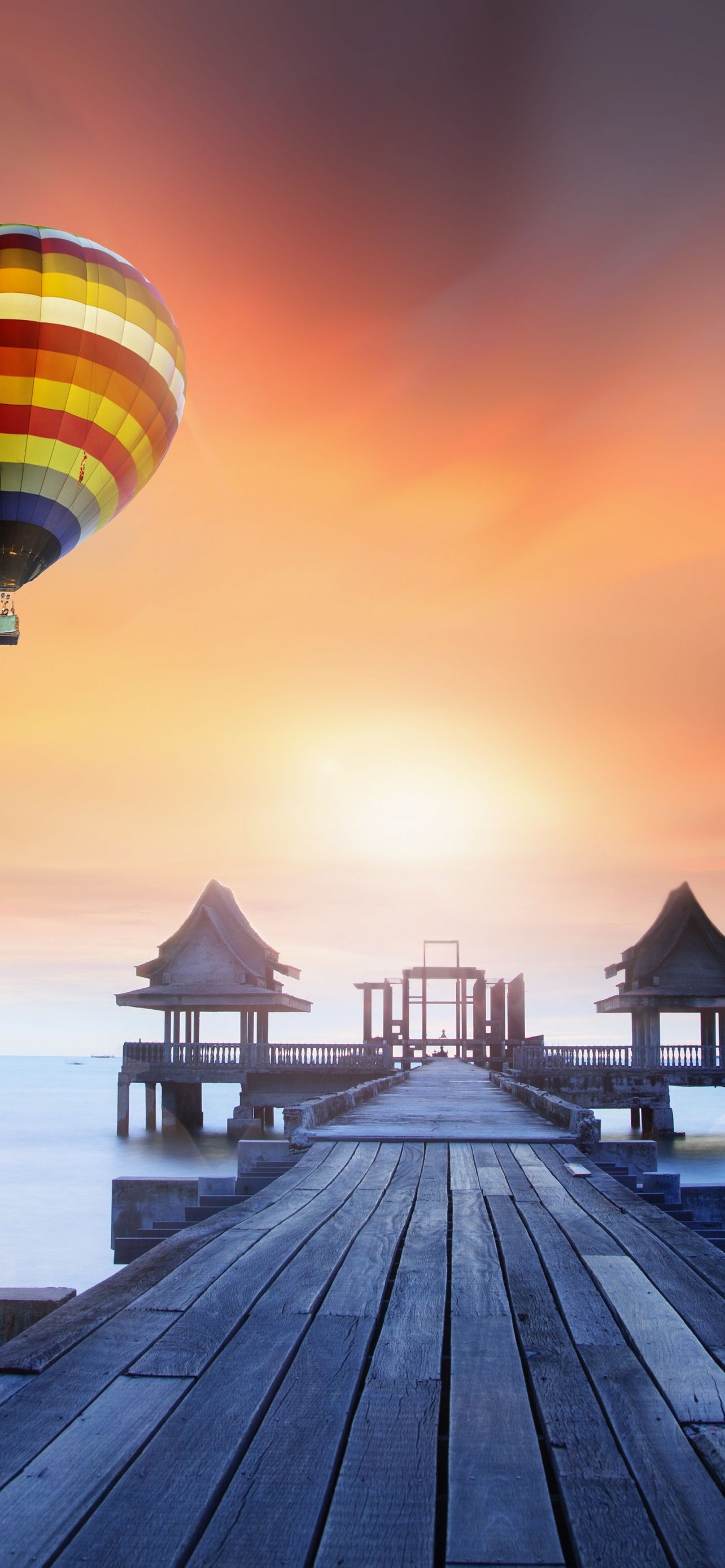 A colorful hot air balloon flying over a wooden pier - Hot air balloons
