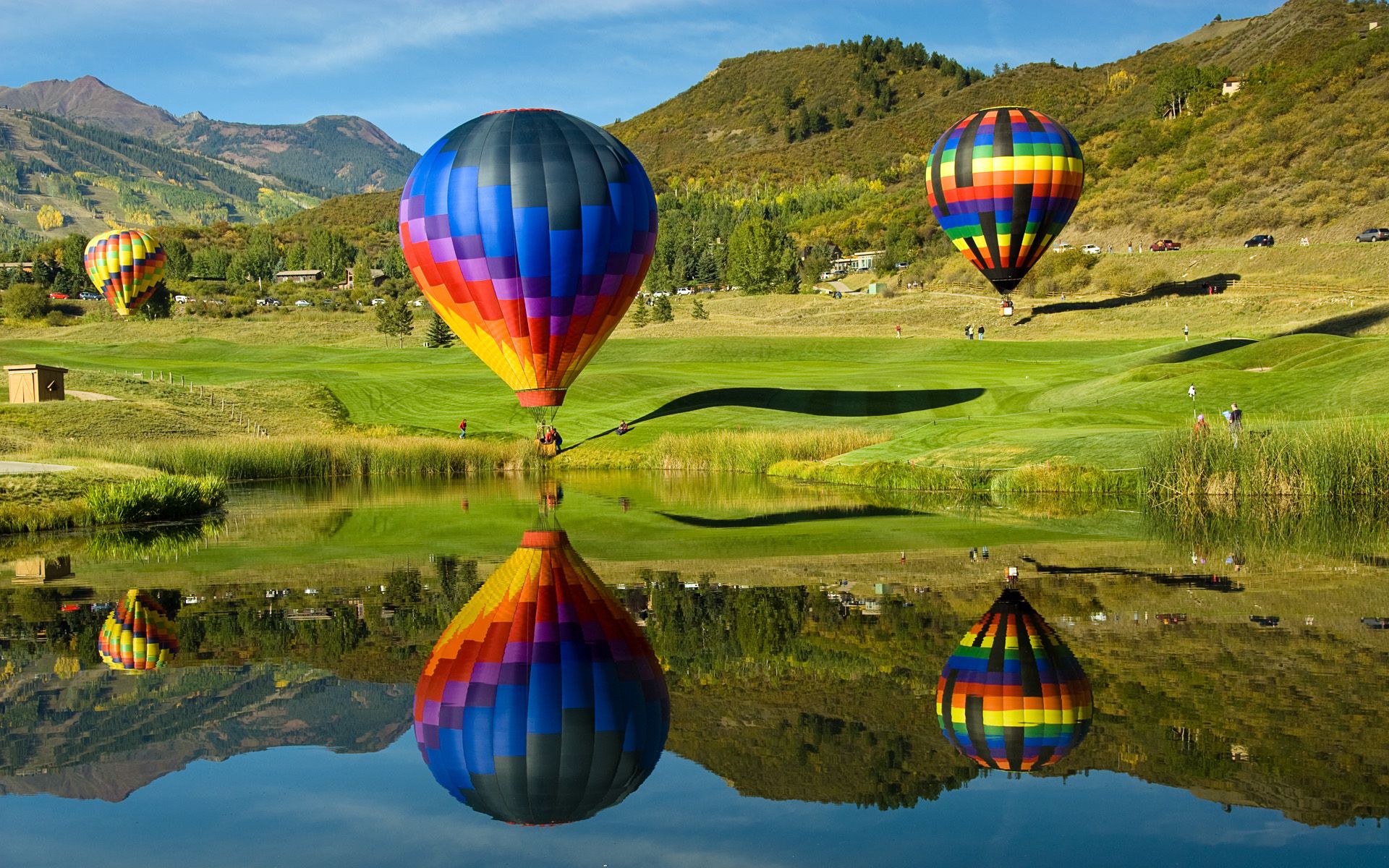 A colorful hot air balloons flying over a green field. - Hot air balloons