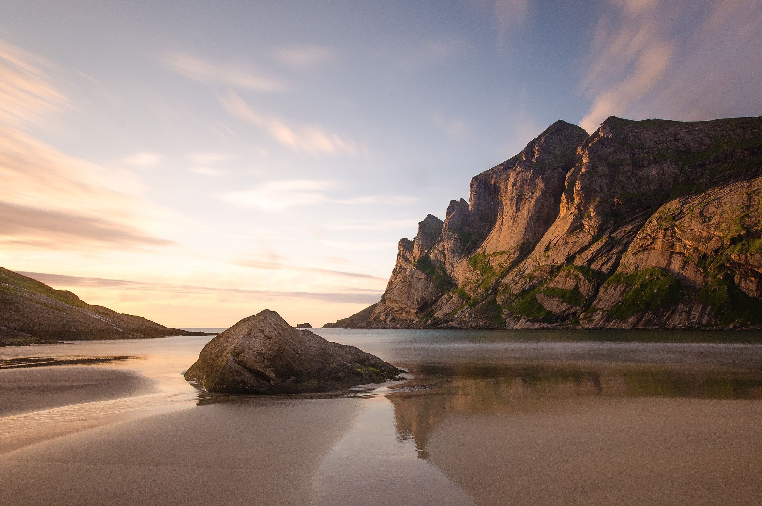 A rocky outcrop sits on a sandy beach at sunset. - Chromebook