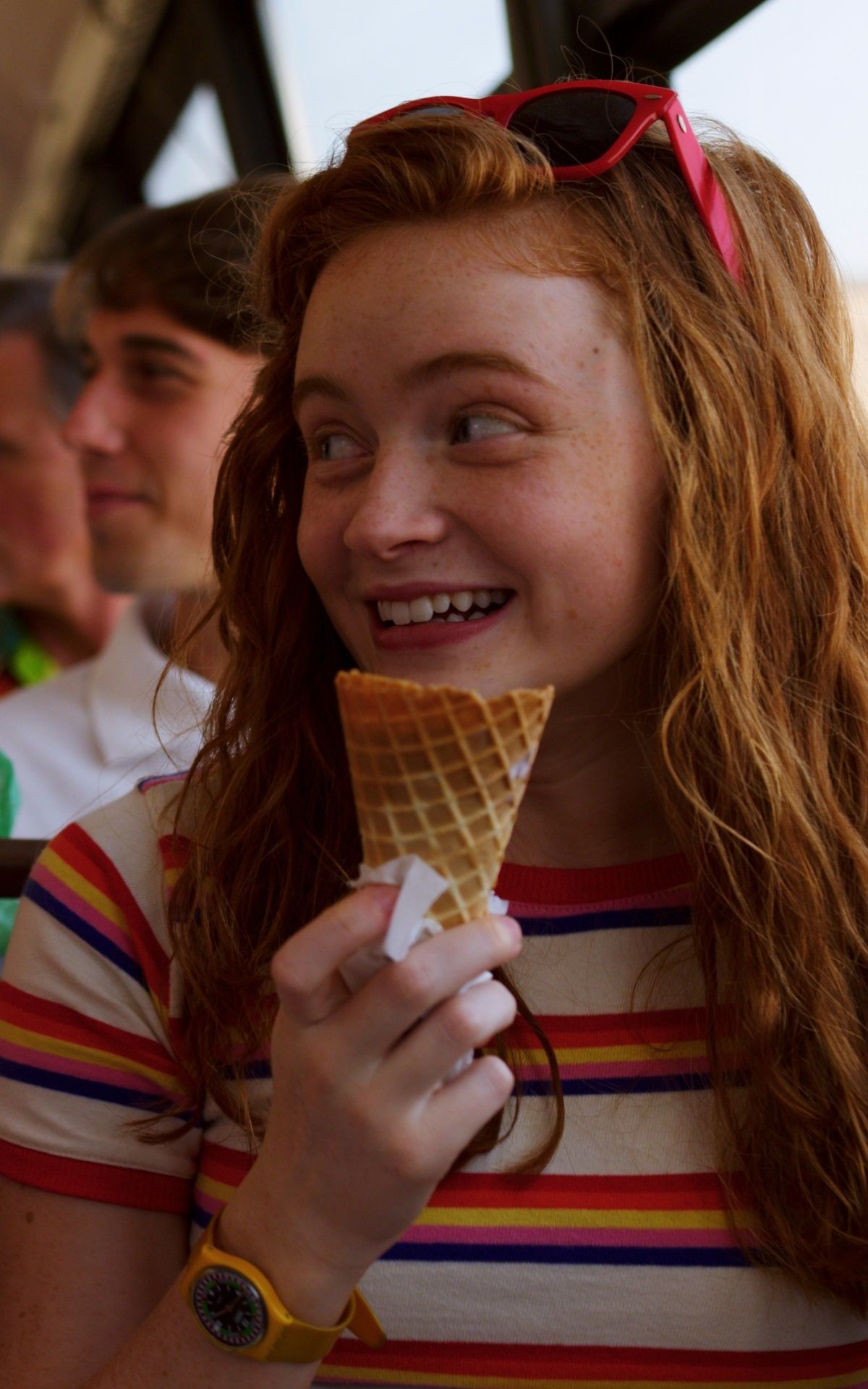 A girl with red hair and a rainbow striped shirt eats an ice cream cone. - Stranger Things