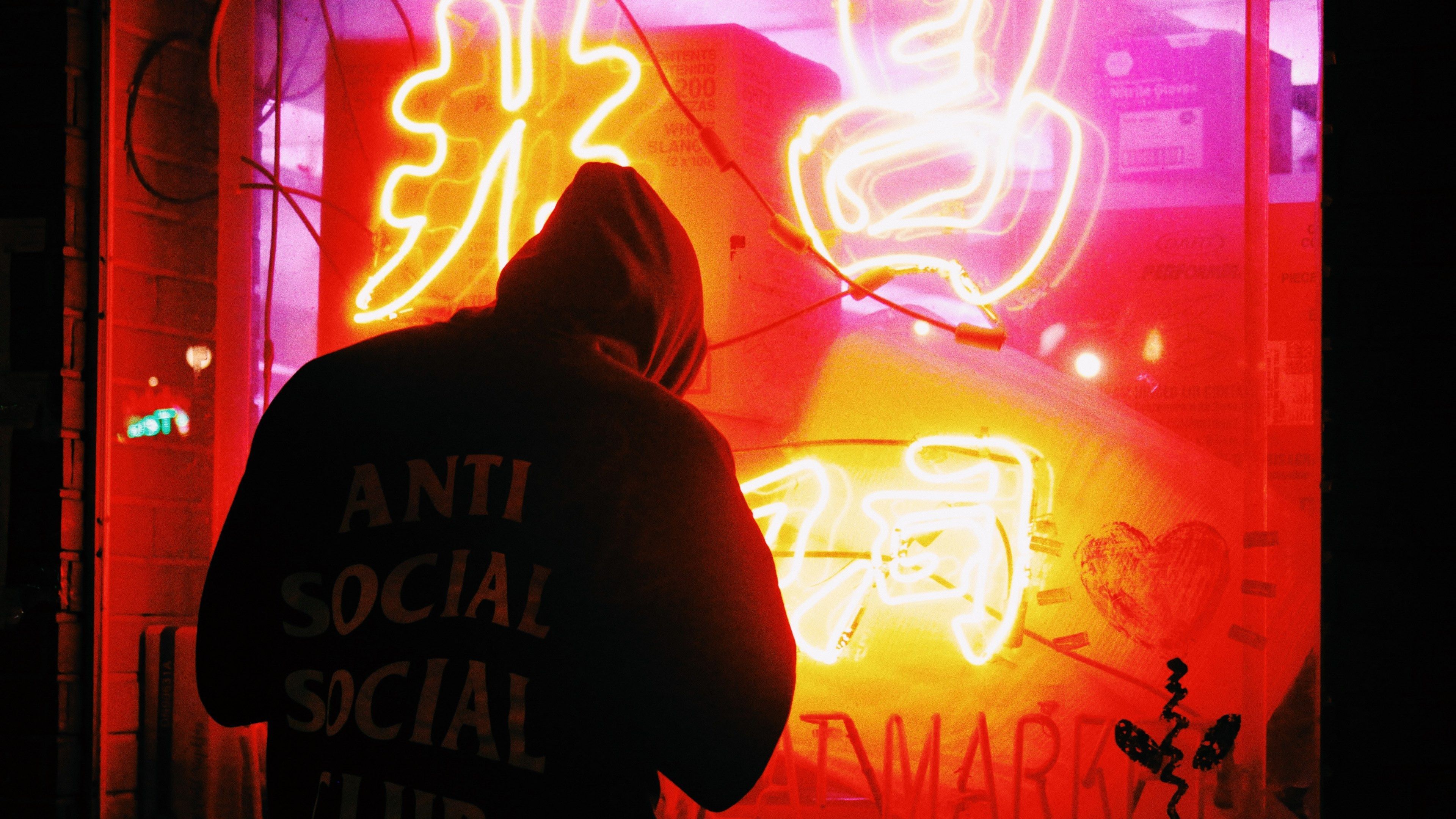 Wallpaper / man in hoody with anti social slogan standing outside red neon display in store window, man red neon window display 4k wallpaper free download
