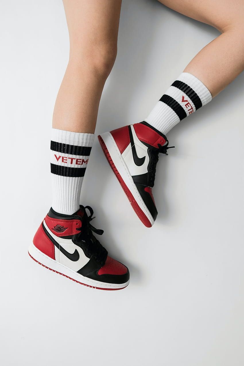 A model wears a pair of black and red sneakers with white socks that say Vetem. - Air Jordan