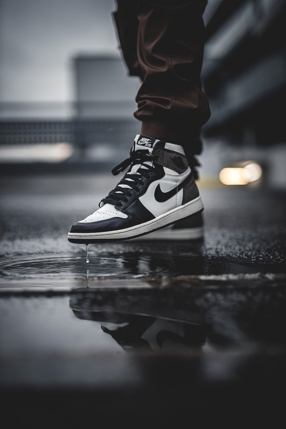 A person wearing black and white Nike Jordan shoes standing on a puddle. - Air Jordan 1, Air Jordan