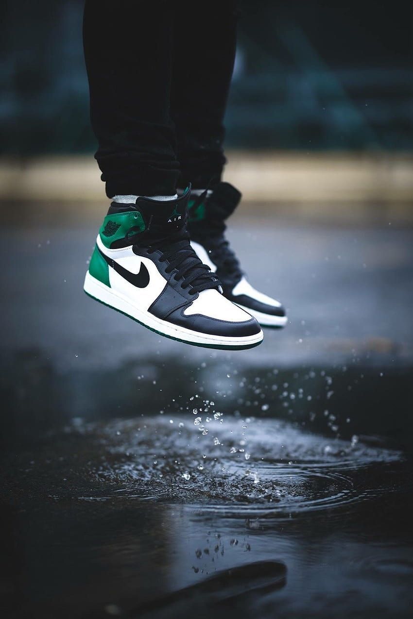 A person jumping in the air wearing black and green sneakers - Air Jordan 1