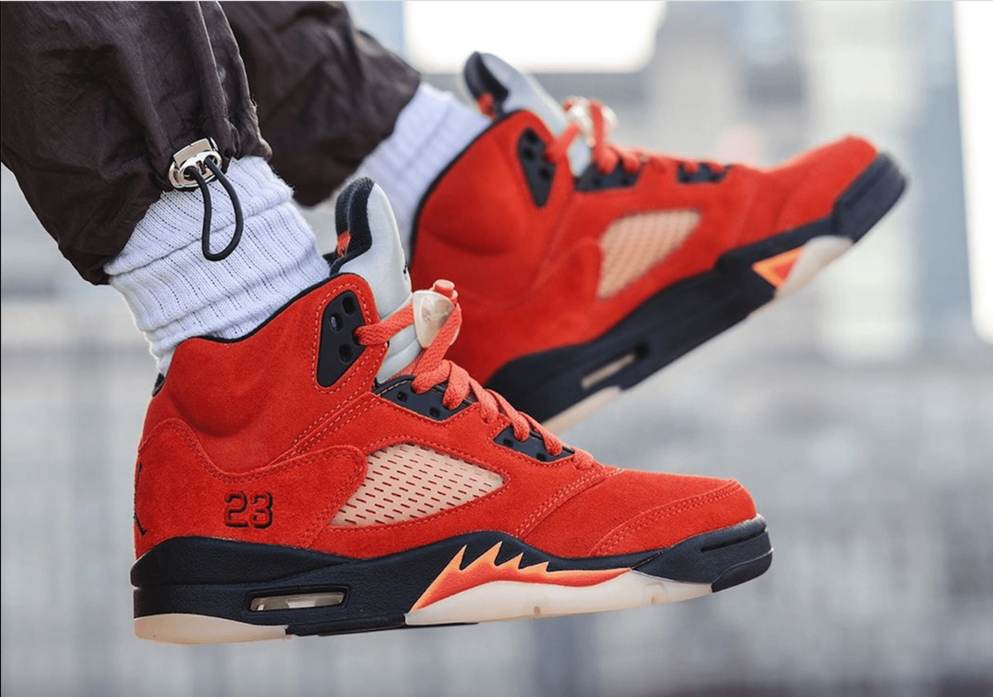 A pair of feet wearing red sneakers with the number 23 on the side. - Air Jordan 5
