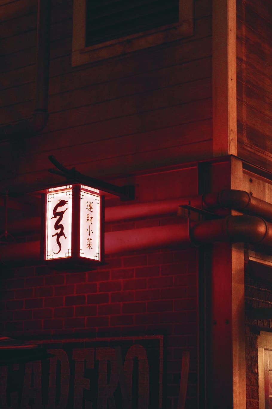 A red neon sign in Chinese characters, hanging from a red brick wall. - Chinese