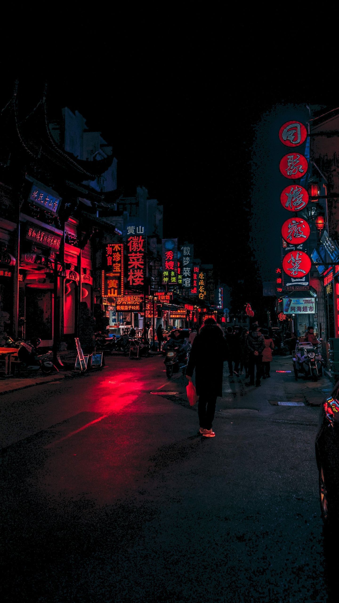 A person walking down a street at night with red neon signs. - Chinese