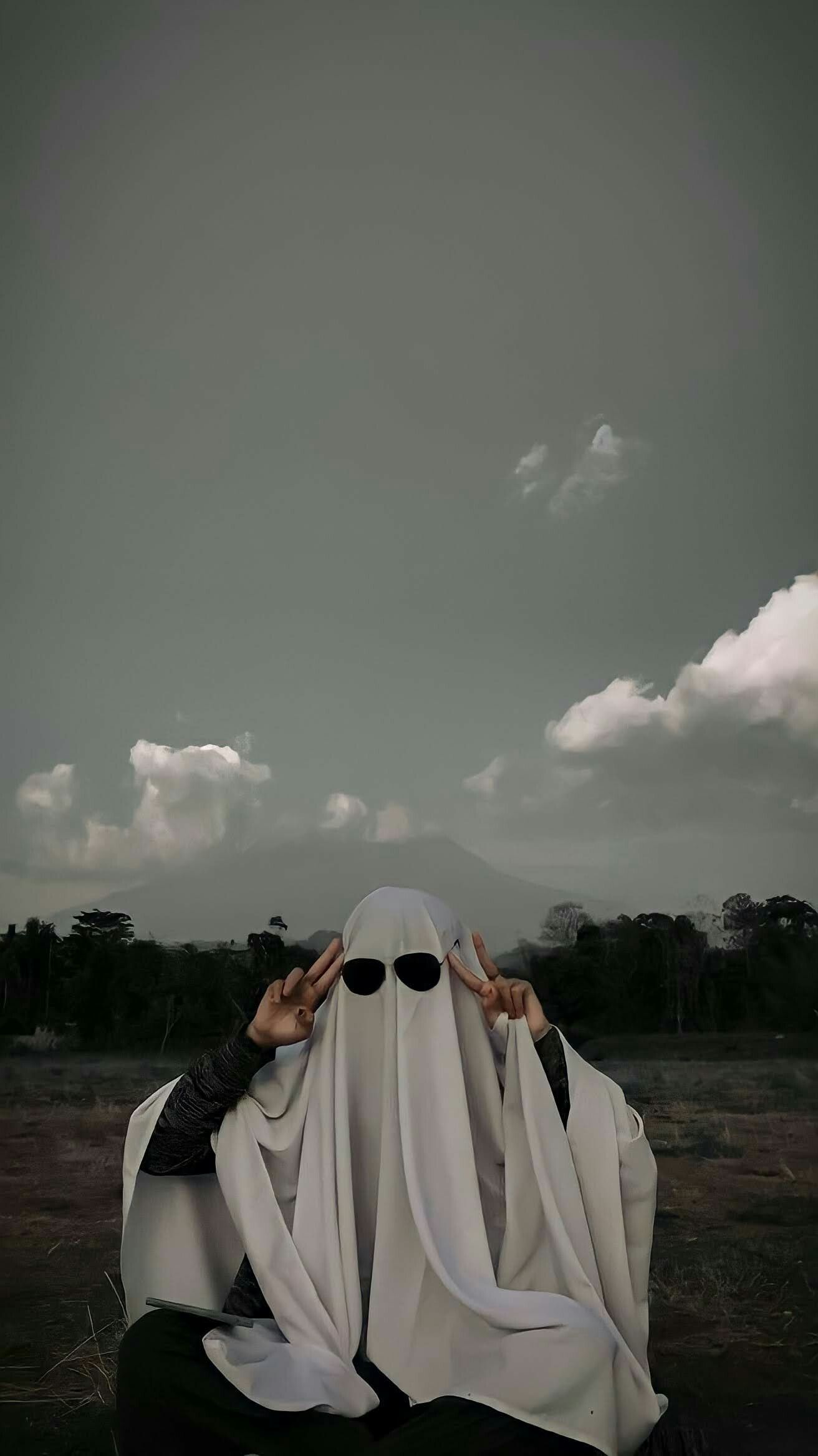 Two people in white ghost costumes sit on a hill. - Ghost