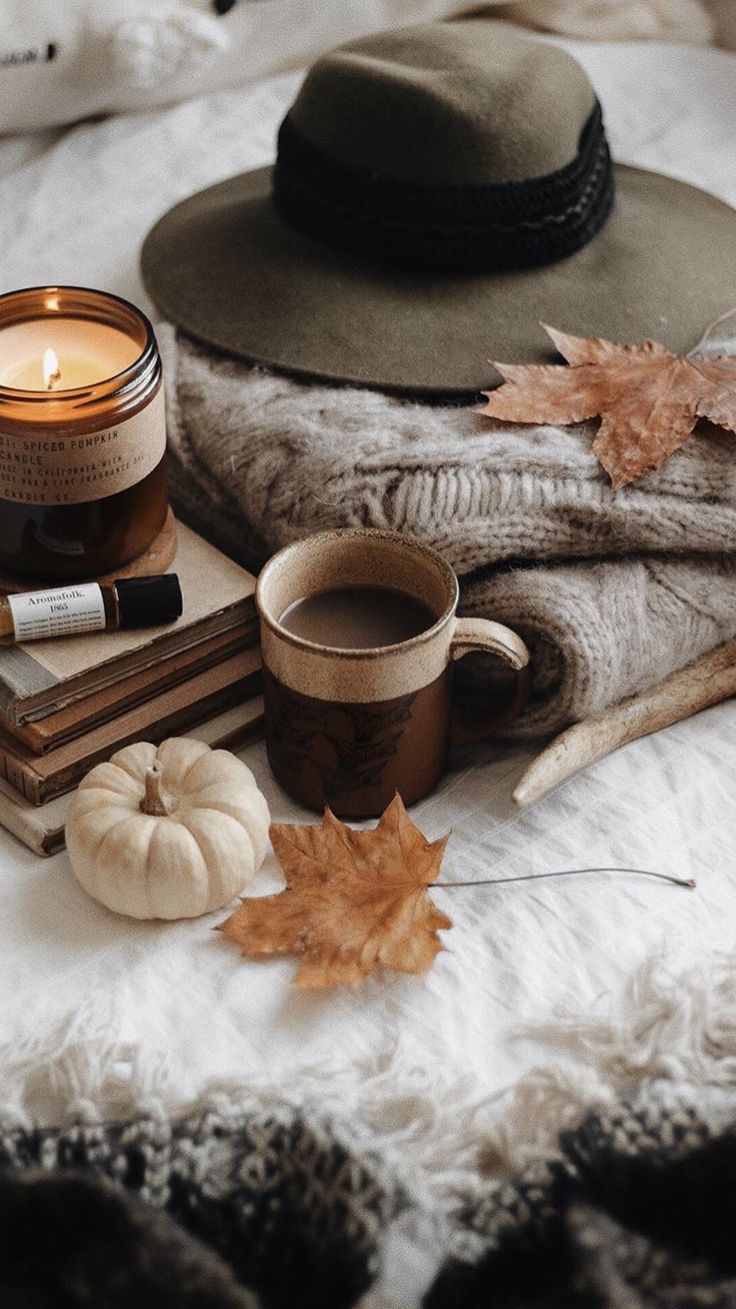 Cozy fall flatlay with a cup of coffee, a candle, a hat, a stack of books, and a pumpkin. - Cozy