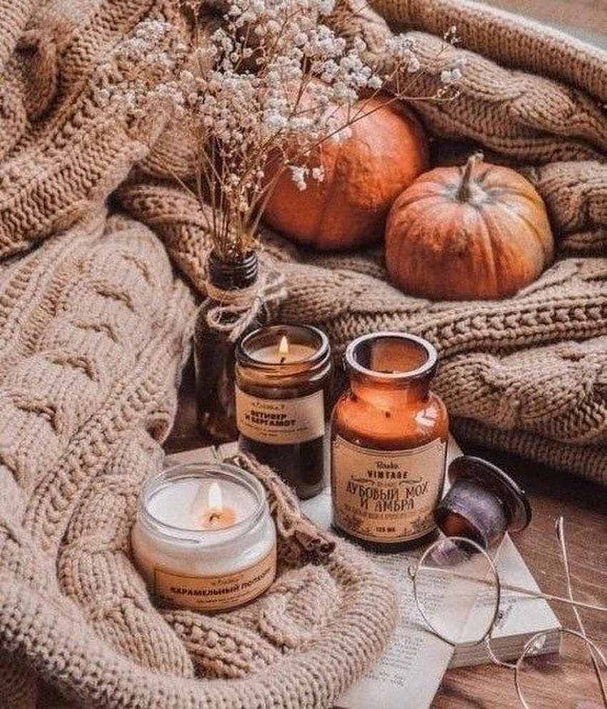 A few candles sit on a blanket with a pumpkin and flowers. - Cozy