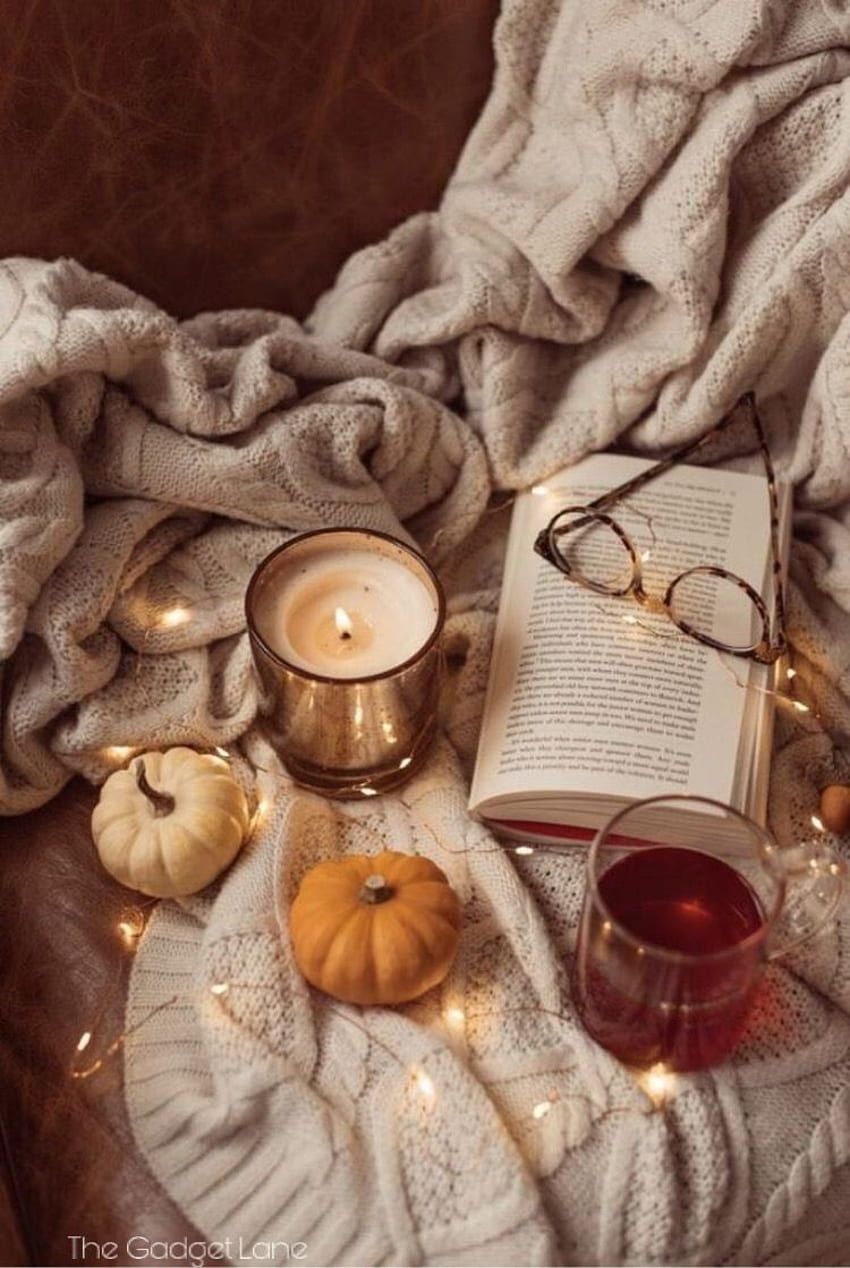 A cozy autumn scene with a book, a lit candle, a cup of tea, and a pair of glasses. - Cozy