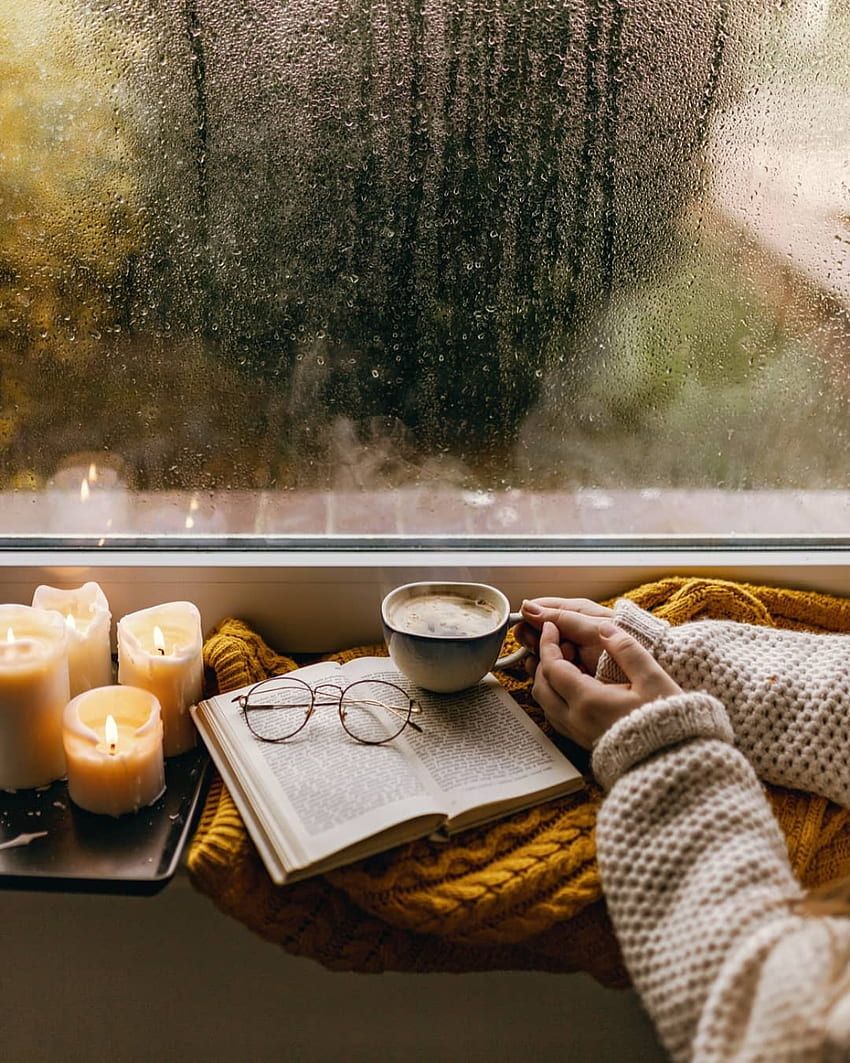 A person reading a book with a cup of coffee and candles. - Cozy