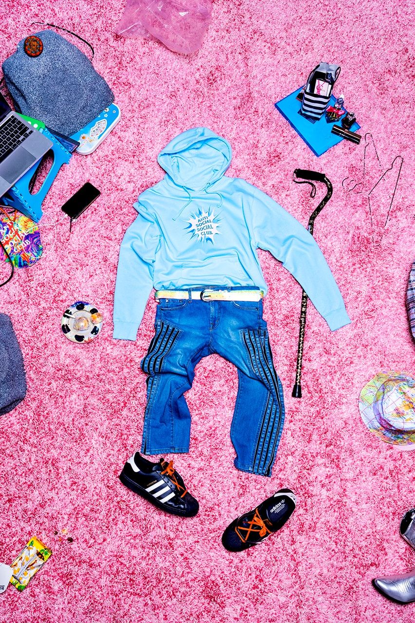 A blue hoodie, jeans, and sneakers lie on a pink carpet. - Anti Social Social Club