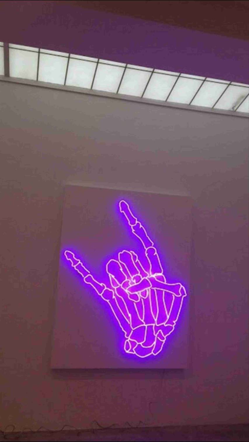 A purple neon sign of a skeleton hand giving the hang loose hand sign - Neon