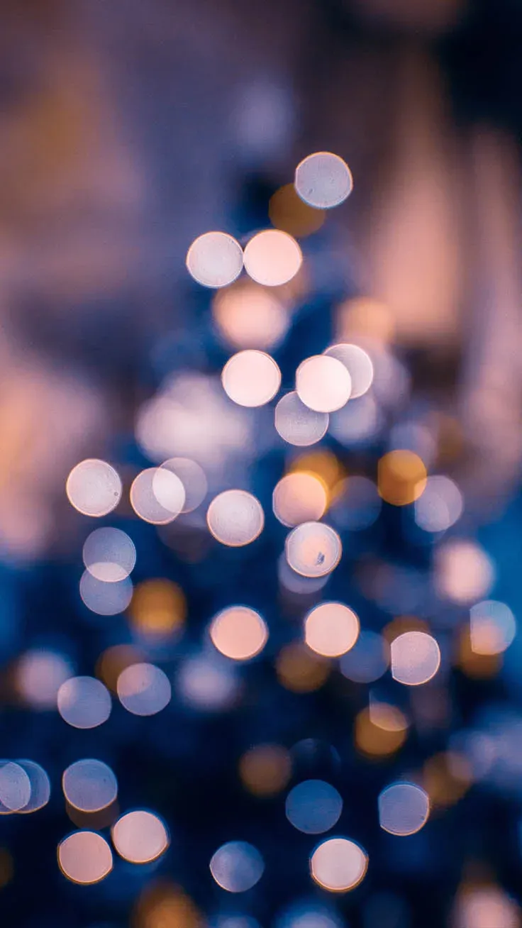 A blurry image of a Christmas tree with white and gold lights. - Christmas iPhone