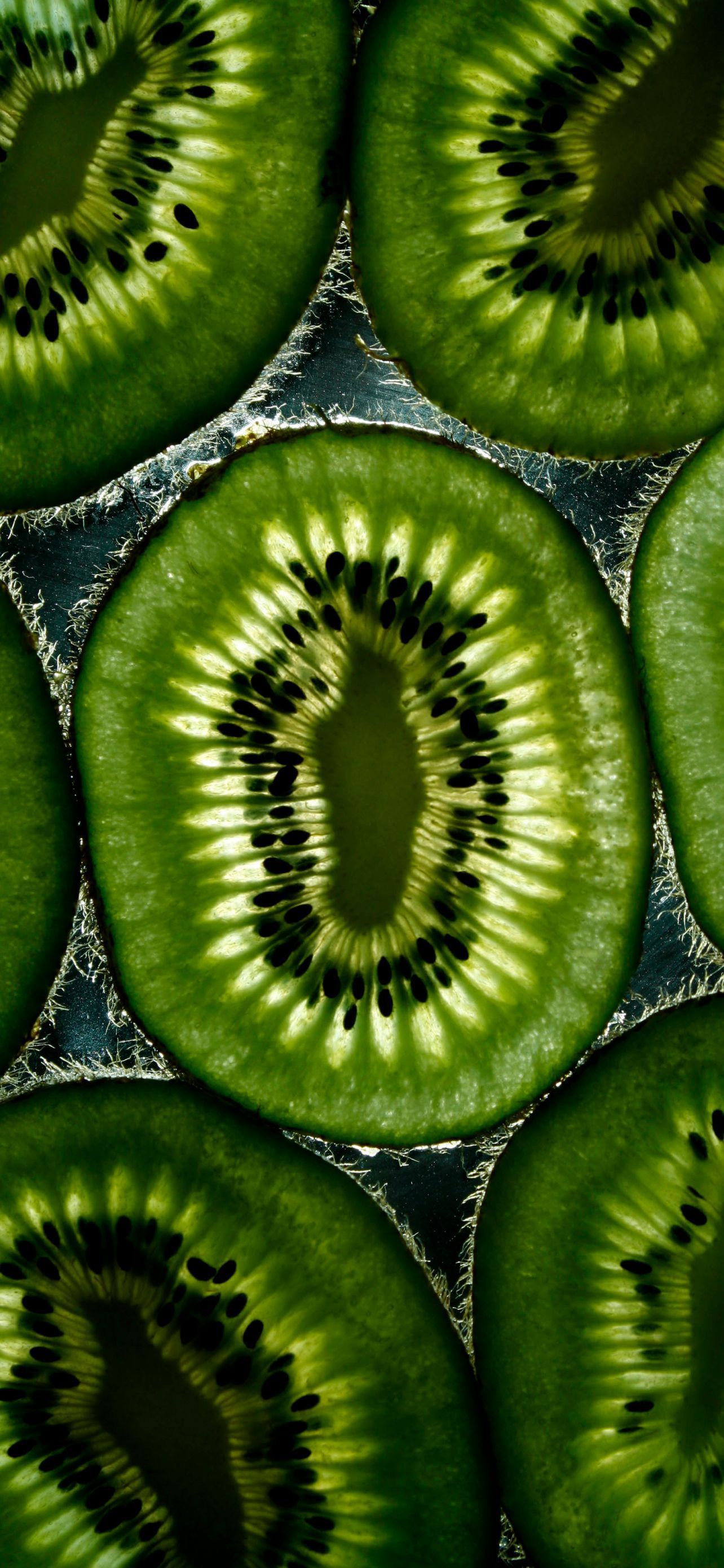 A close up of sliced kiwi fruit on a dark background. - Kiwi