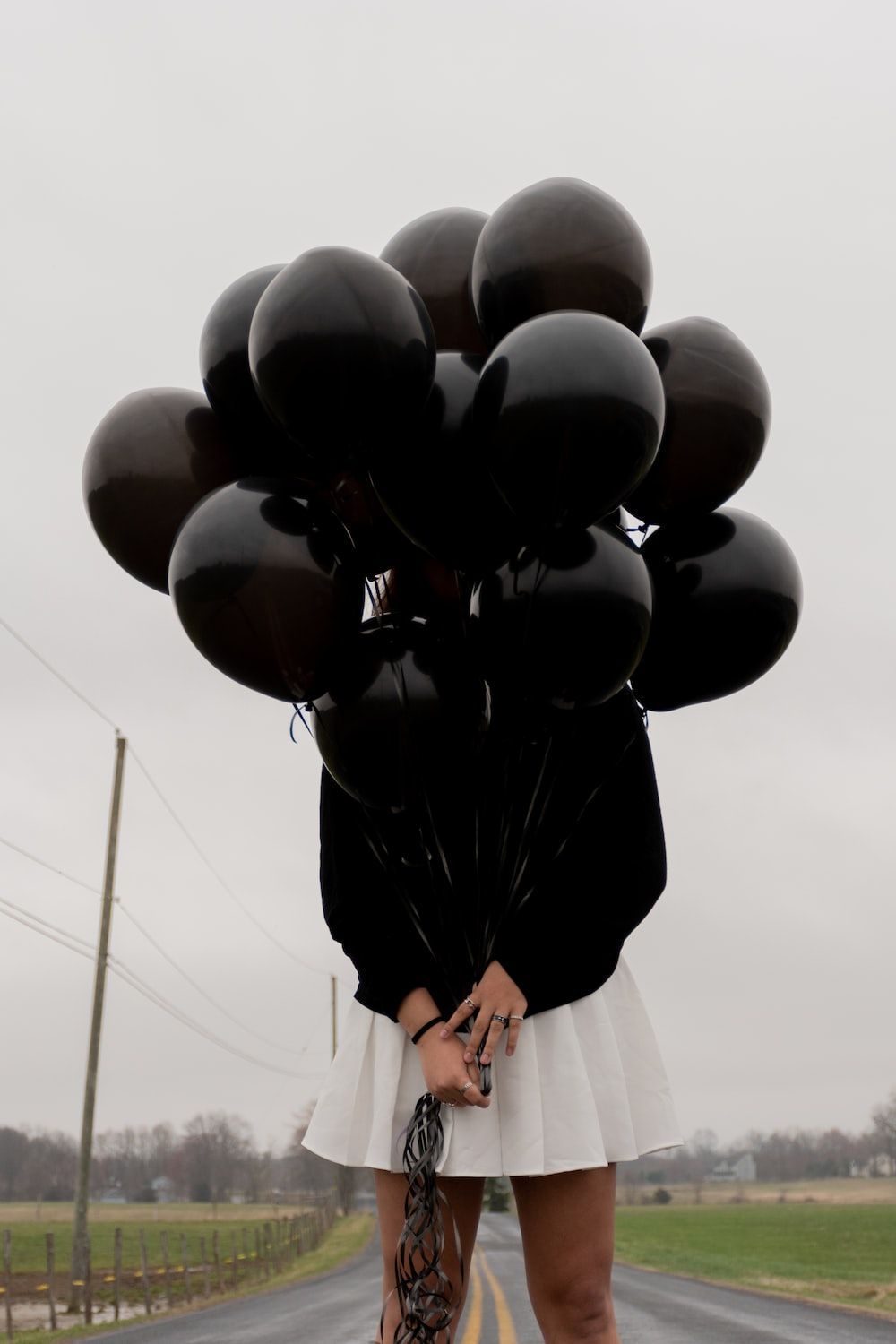A woman holding black balloons on a road - Balloons