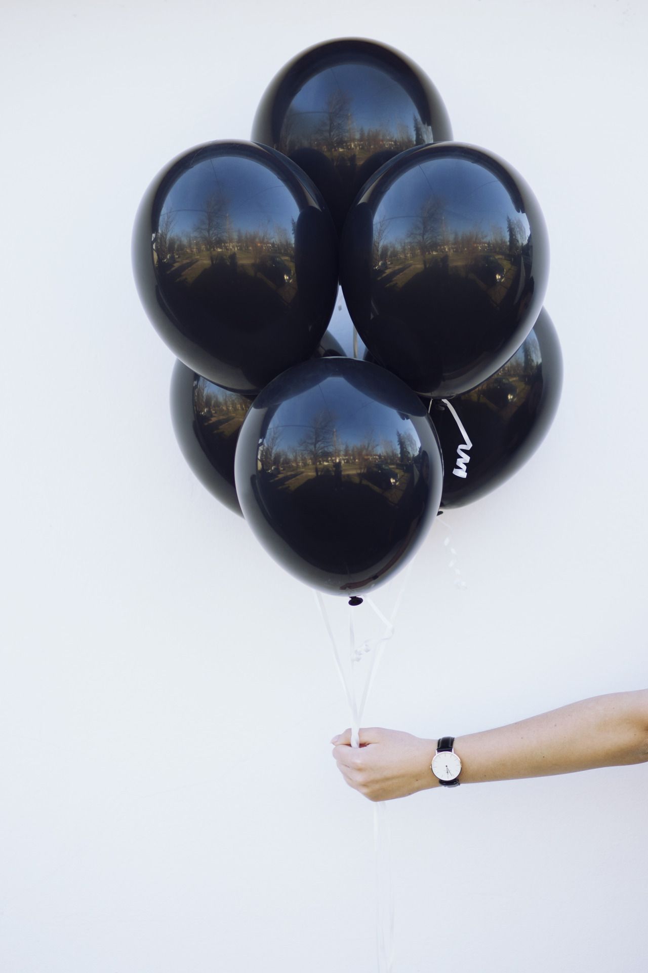A person holding a bunch of black balloons against a white wall - Balloons