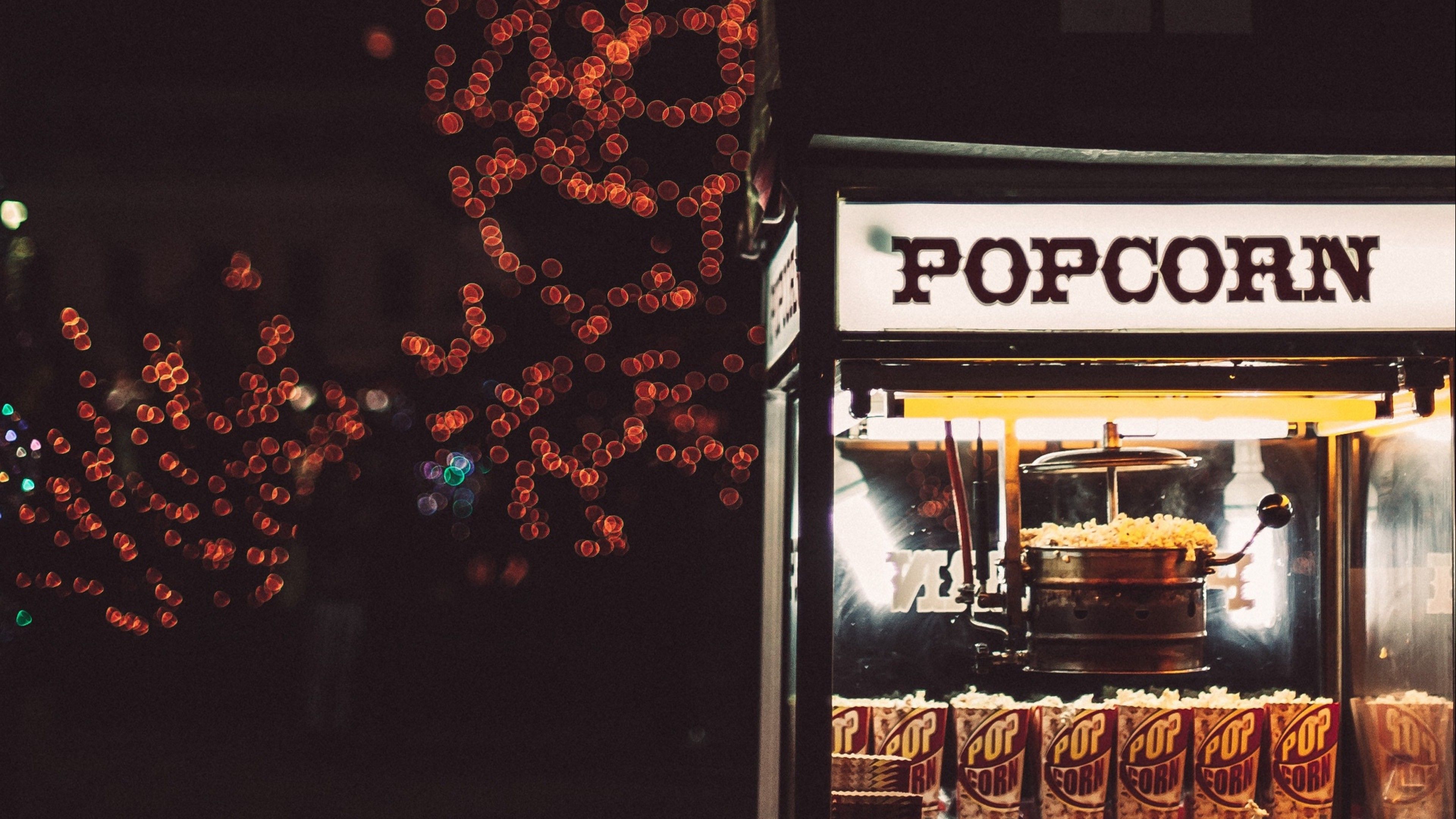 A popcorn stand with a sign that says popcorn and lights in the background. - Popcorn