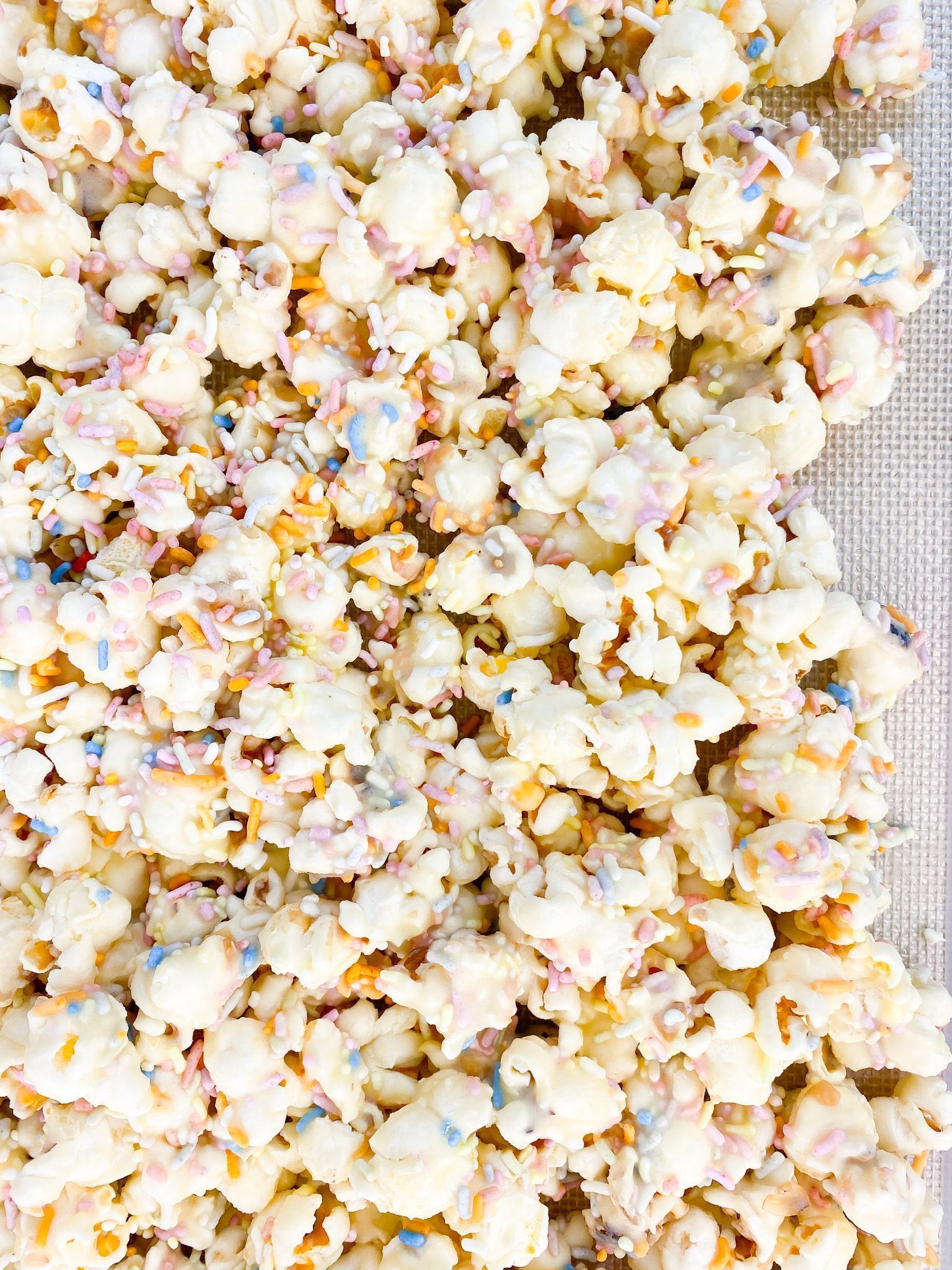 Popcorn covered in white chocolate and sprinkles on a baking sheet. - Popcorn