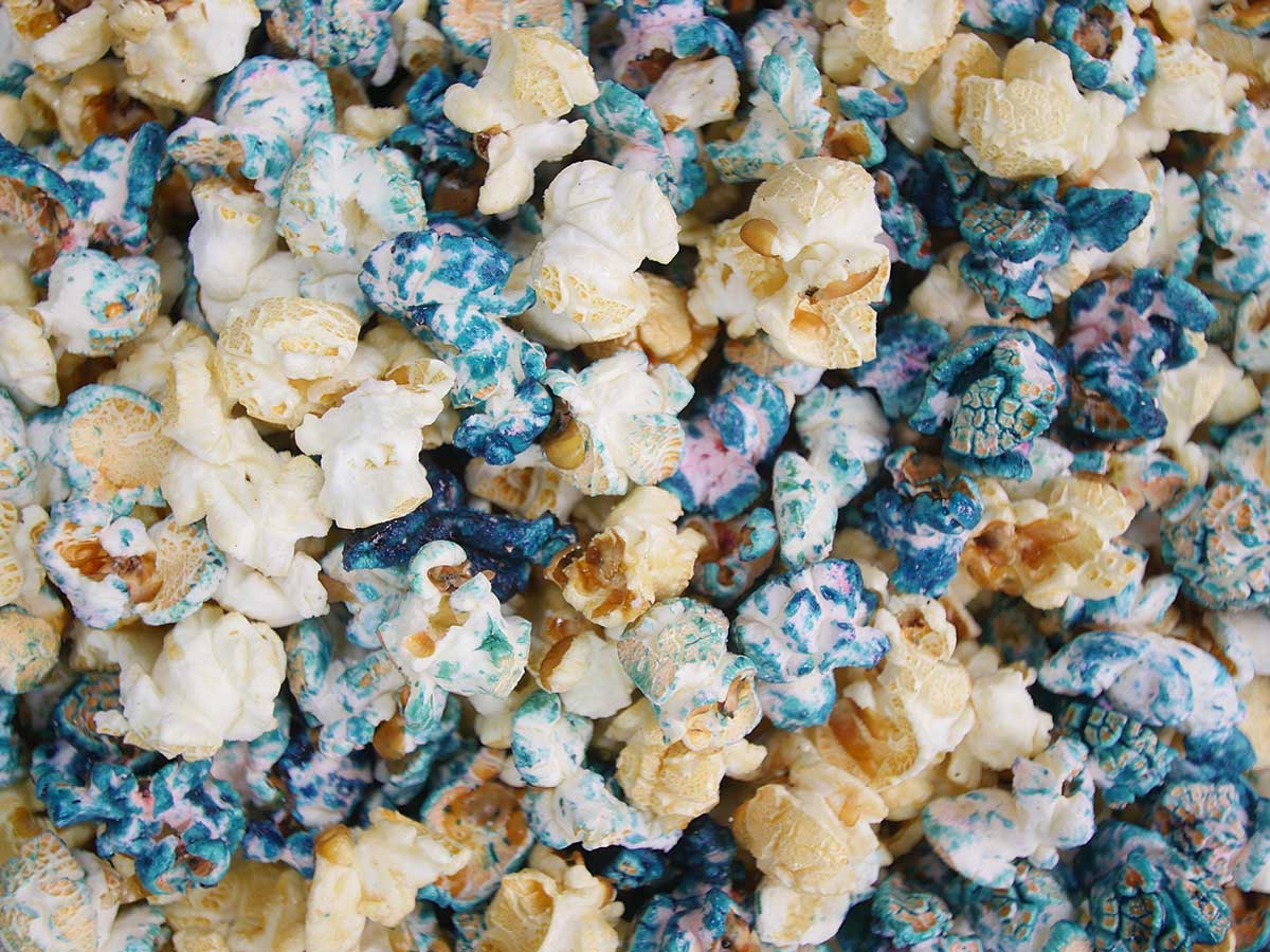 A close up of popcorn with blue and white candy coating. - Popcorn