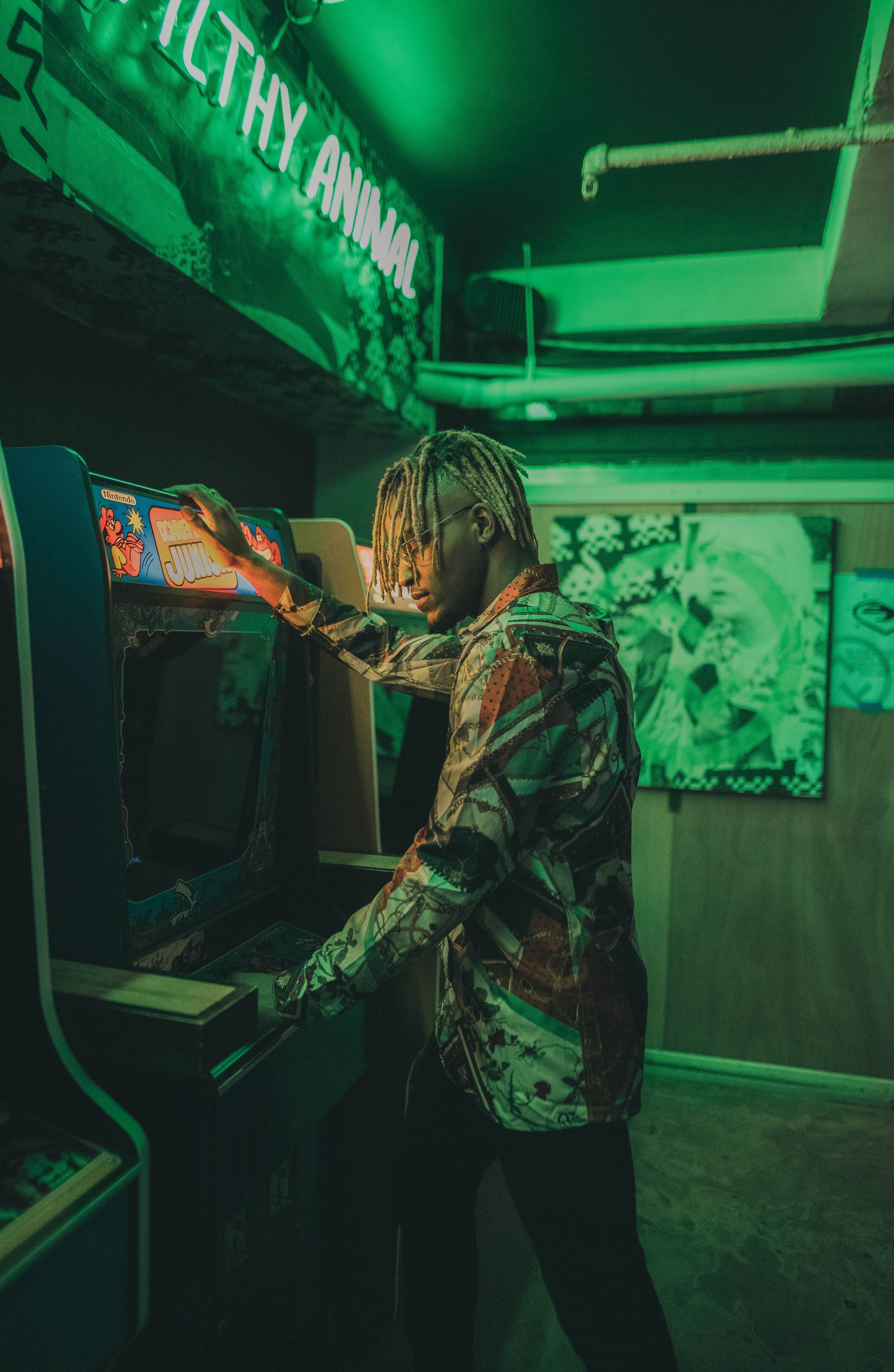 A man in a green lit room playing an arcade game - Arcade