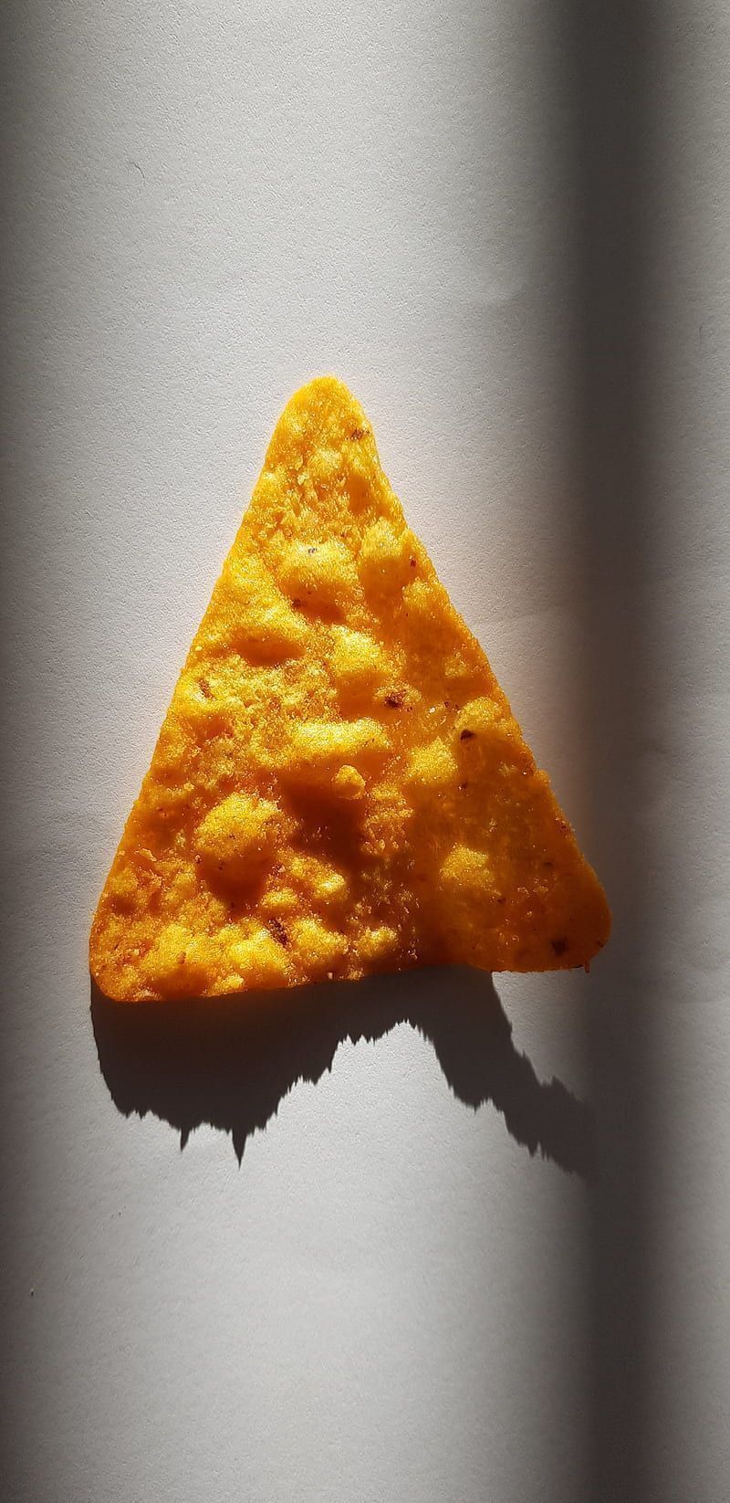 A single corn chip on a white background with a shadow - Doritos