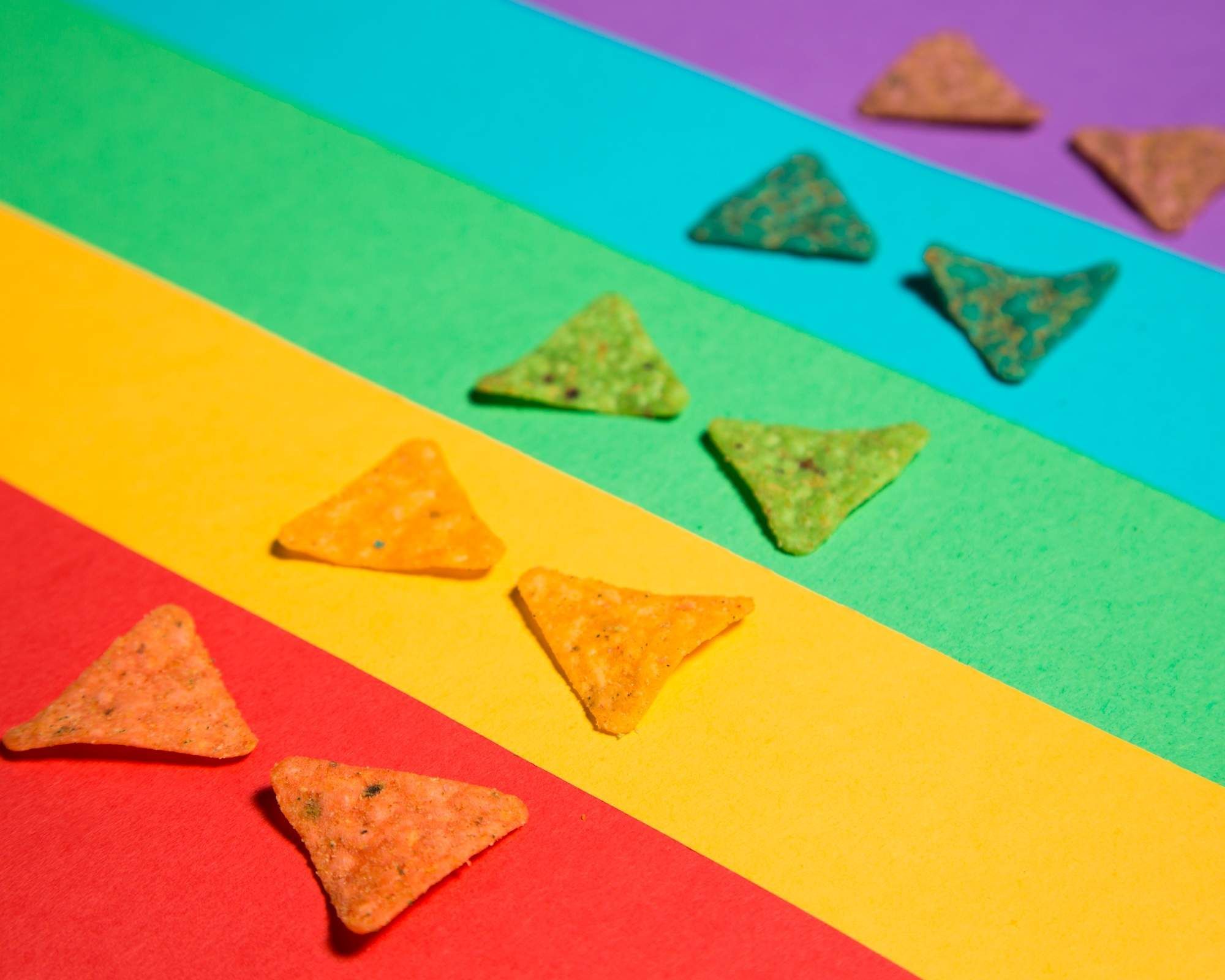 A photo of colorful tortilla chips on a rainbow background. - Doritos