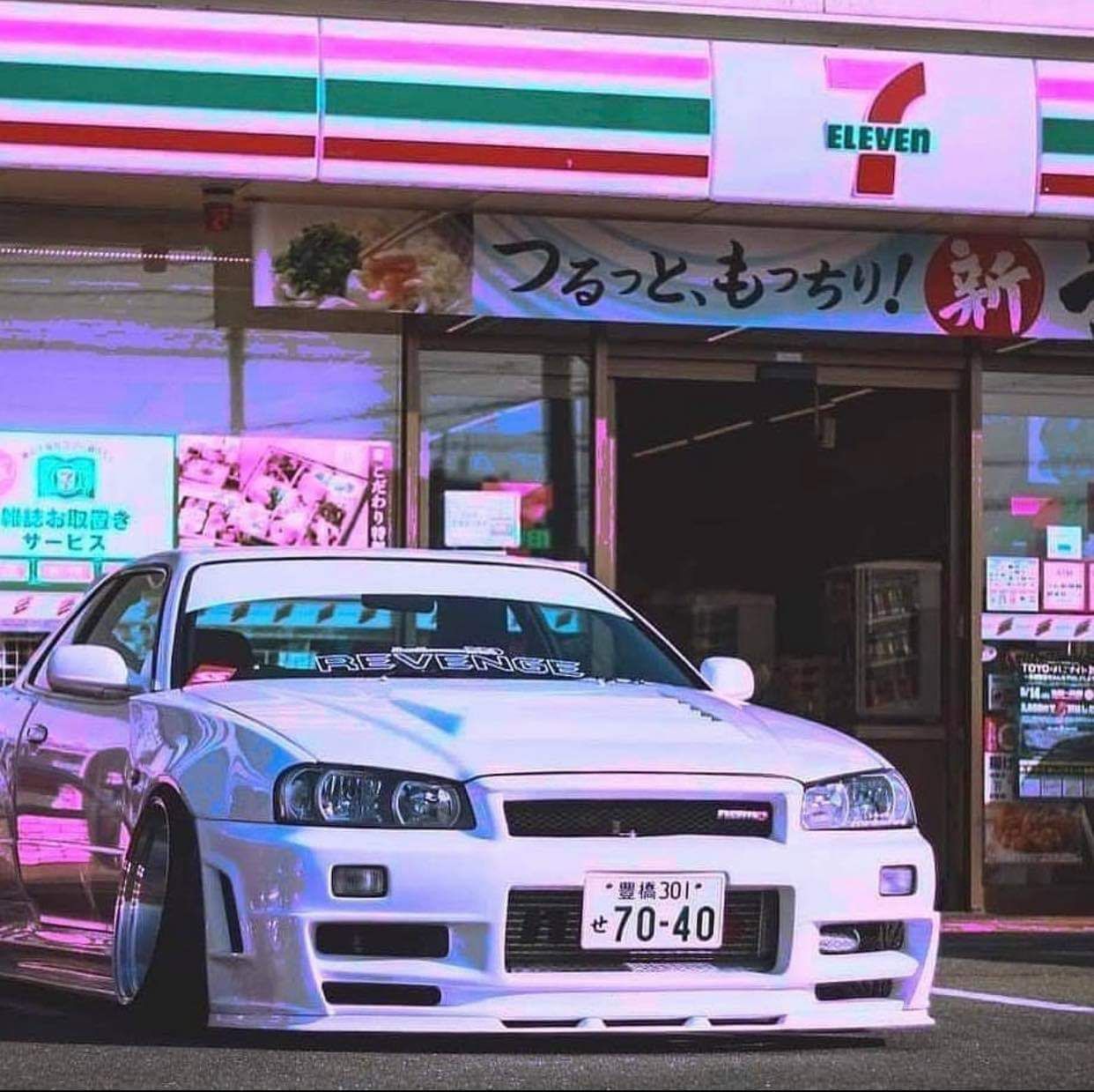 A white car is parked in front of a convenience store. - Nissan Skyline