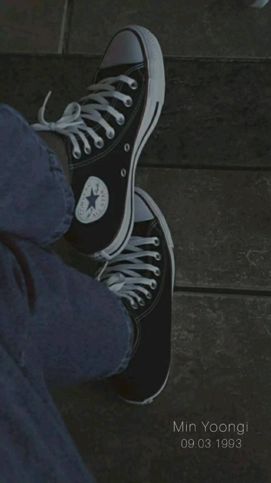 A pair of black converse sneakers with white laces on a wooden floor - Converse