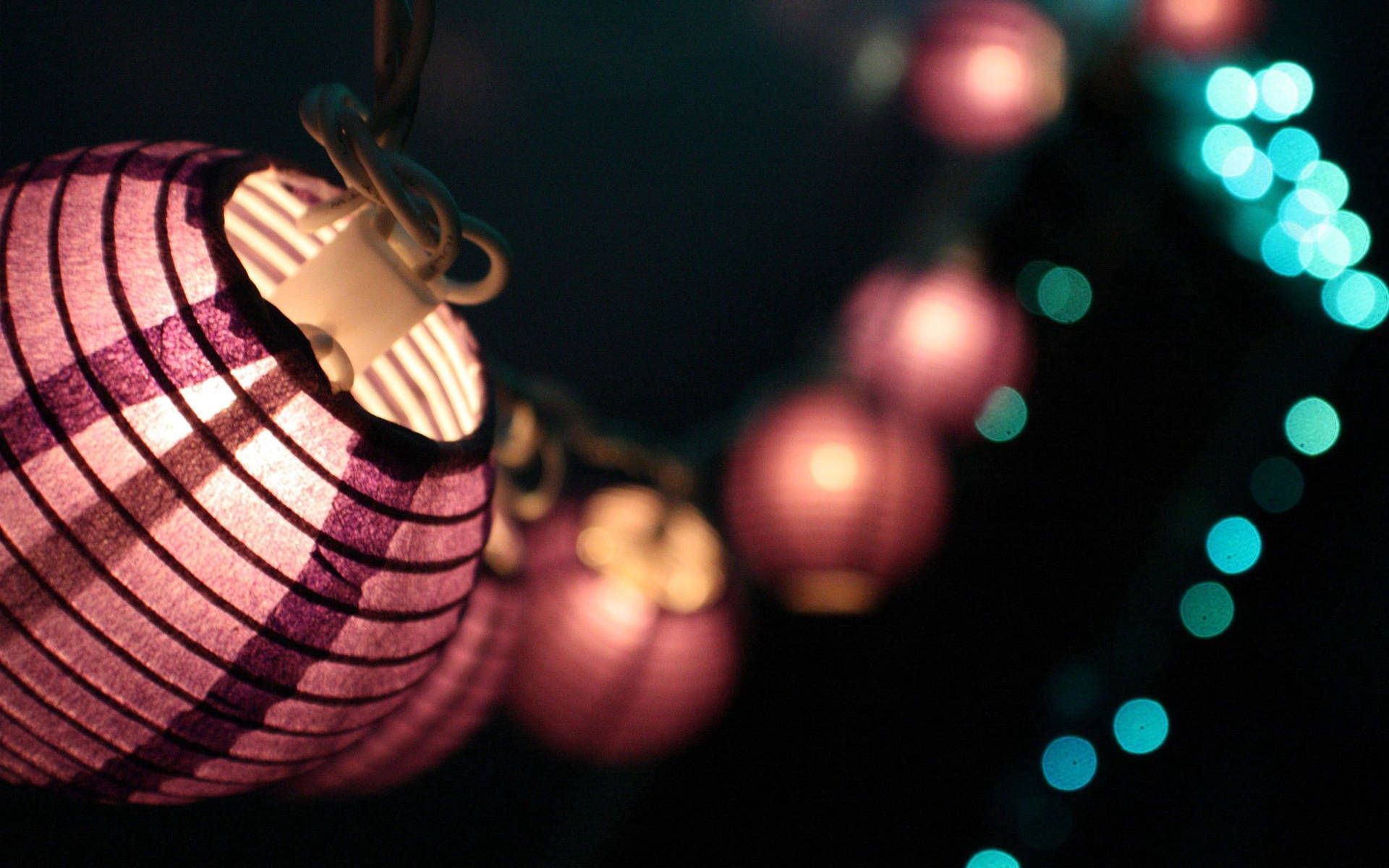 A string of purple, pink and blue paper lanterns against a black background. - Chinese