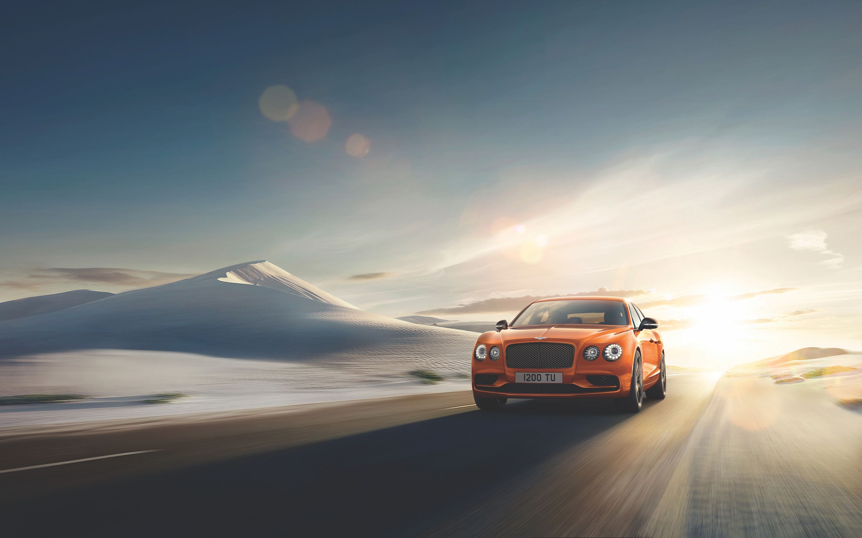 A 2018 Bentley Flying Spur V8 driving on a desert road with the sun setting in the background. - Cars