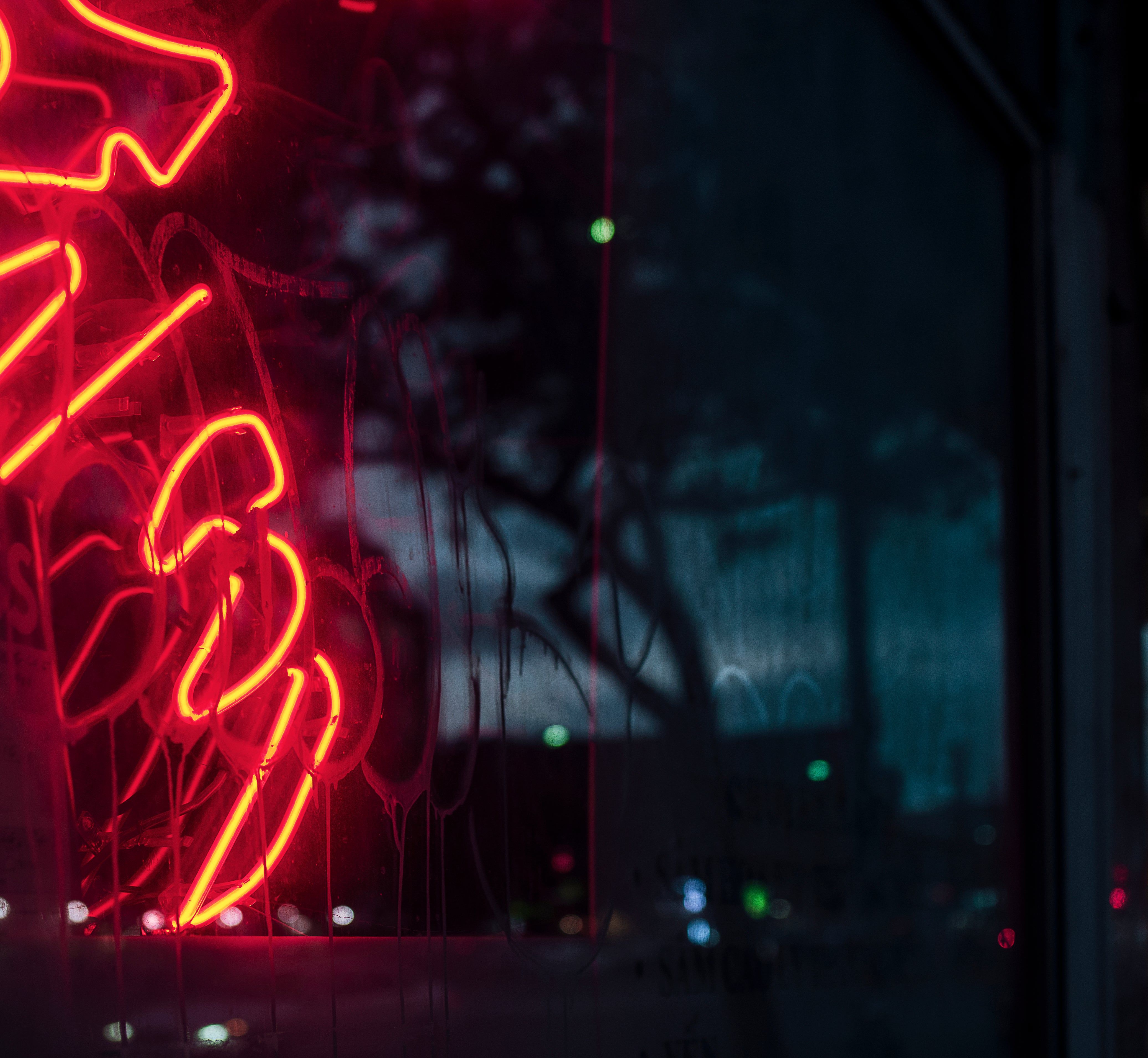 A neon sign reflects on a window at night. - Neon red