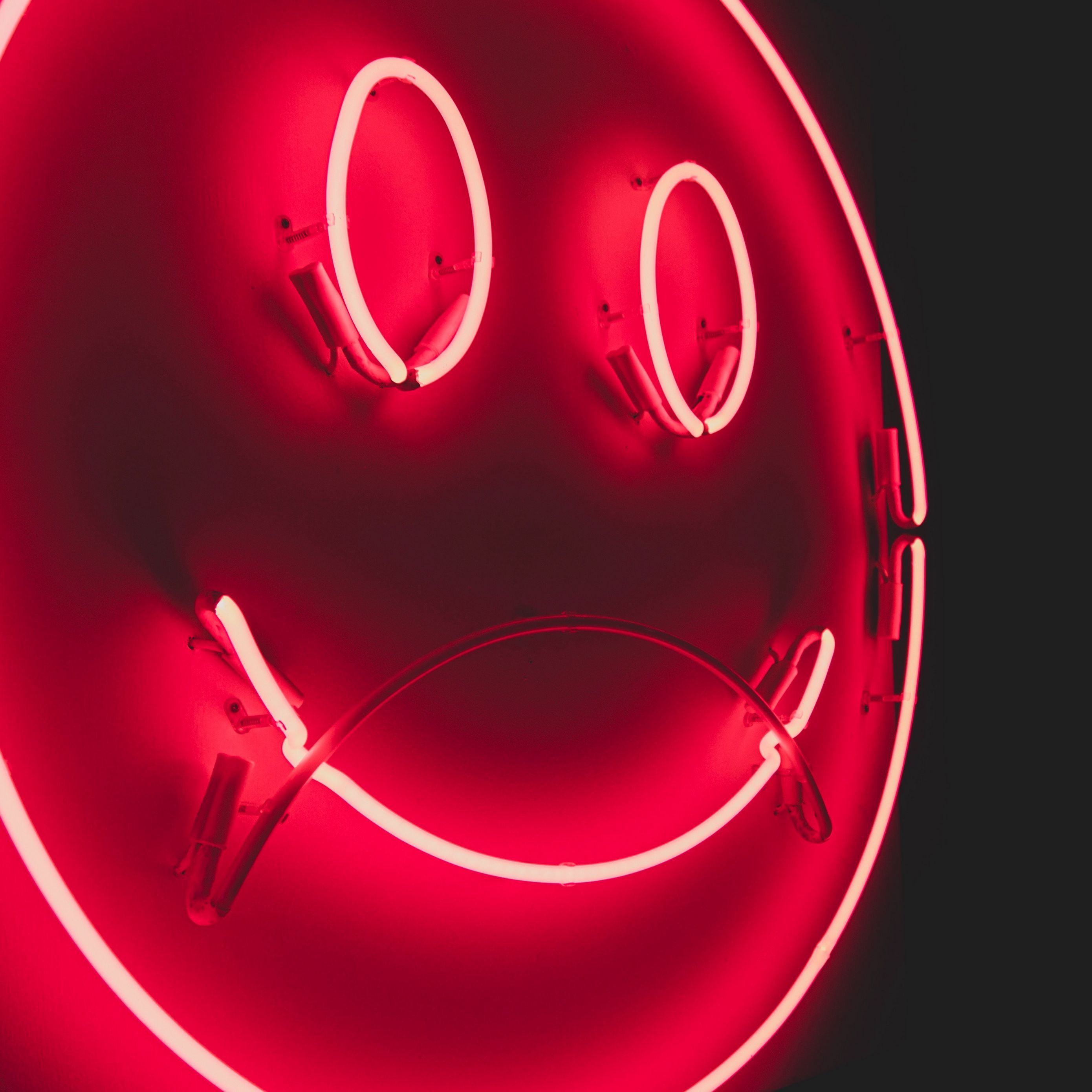 A red neon sign of a sad face. - Neon red