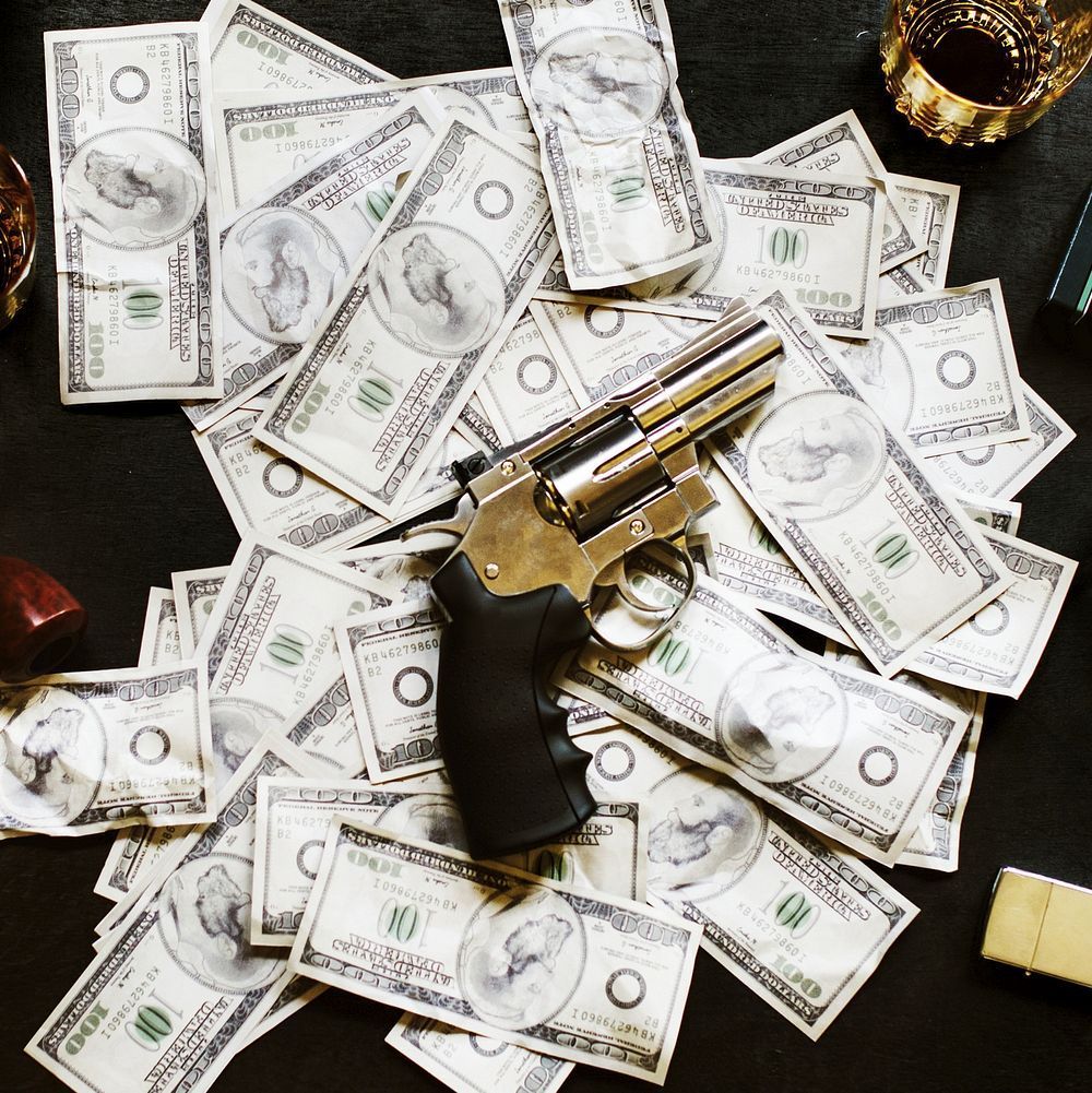 A gun sits on top of a pile of money. - Money