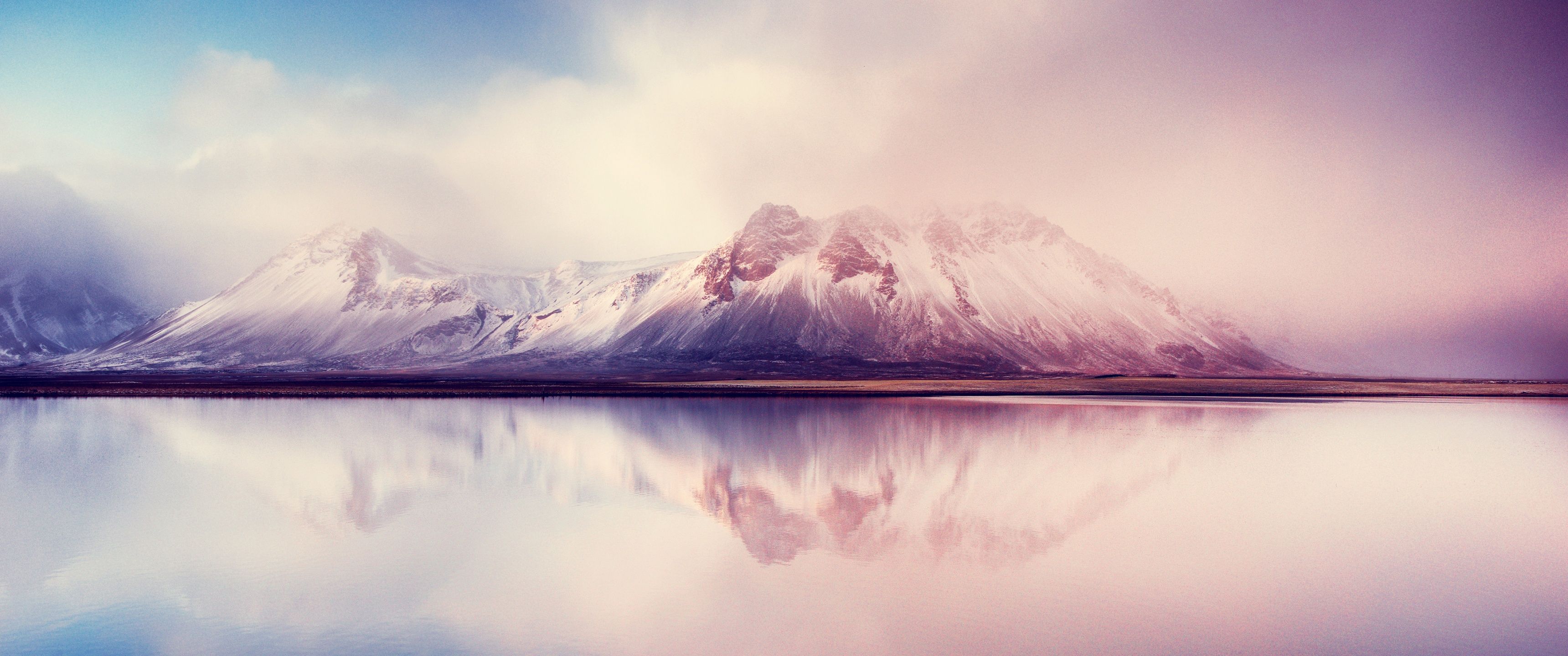 A serene mountain range is reflected in a calm lake, under a cloudy sky in this beautiful image. The snow-capped peaks of the mountains are a sight to behold, with the mist adding to the mystical atmosphere. This is a perfect representation of the beauty of nature, and a must-see for all nature lovers. - 3440x1440, lake, mountain
