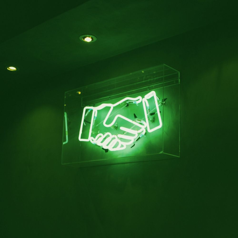 A neon sign of two hands shaking in the dark. - Neon green