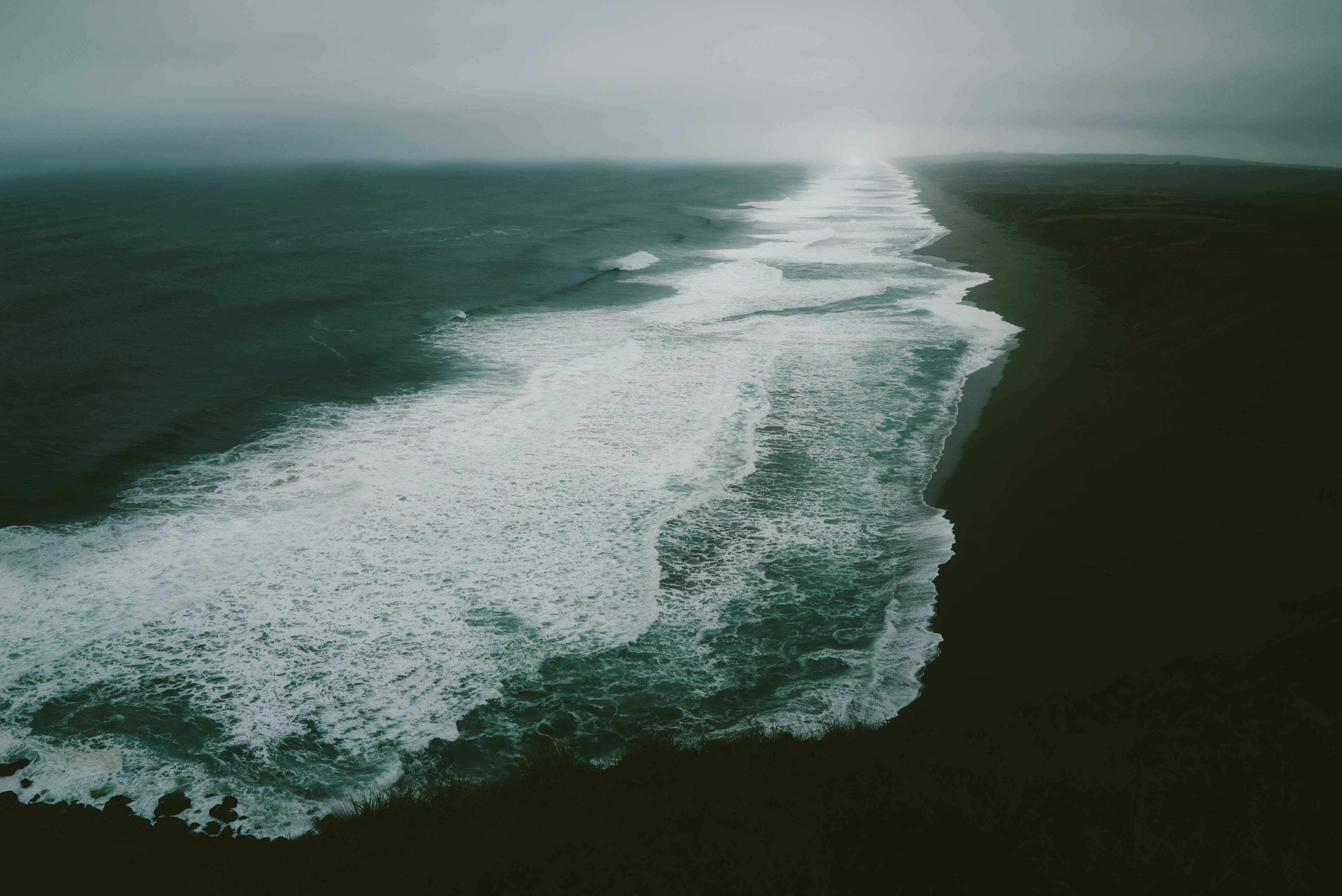 A black sand beach with white foaming waves coming in. - Ocean