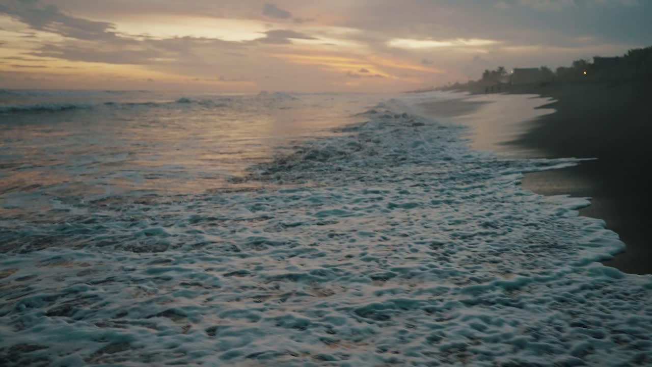 Aerial view of a beach at sunset with waves crashing on the shore. - Ocean