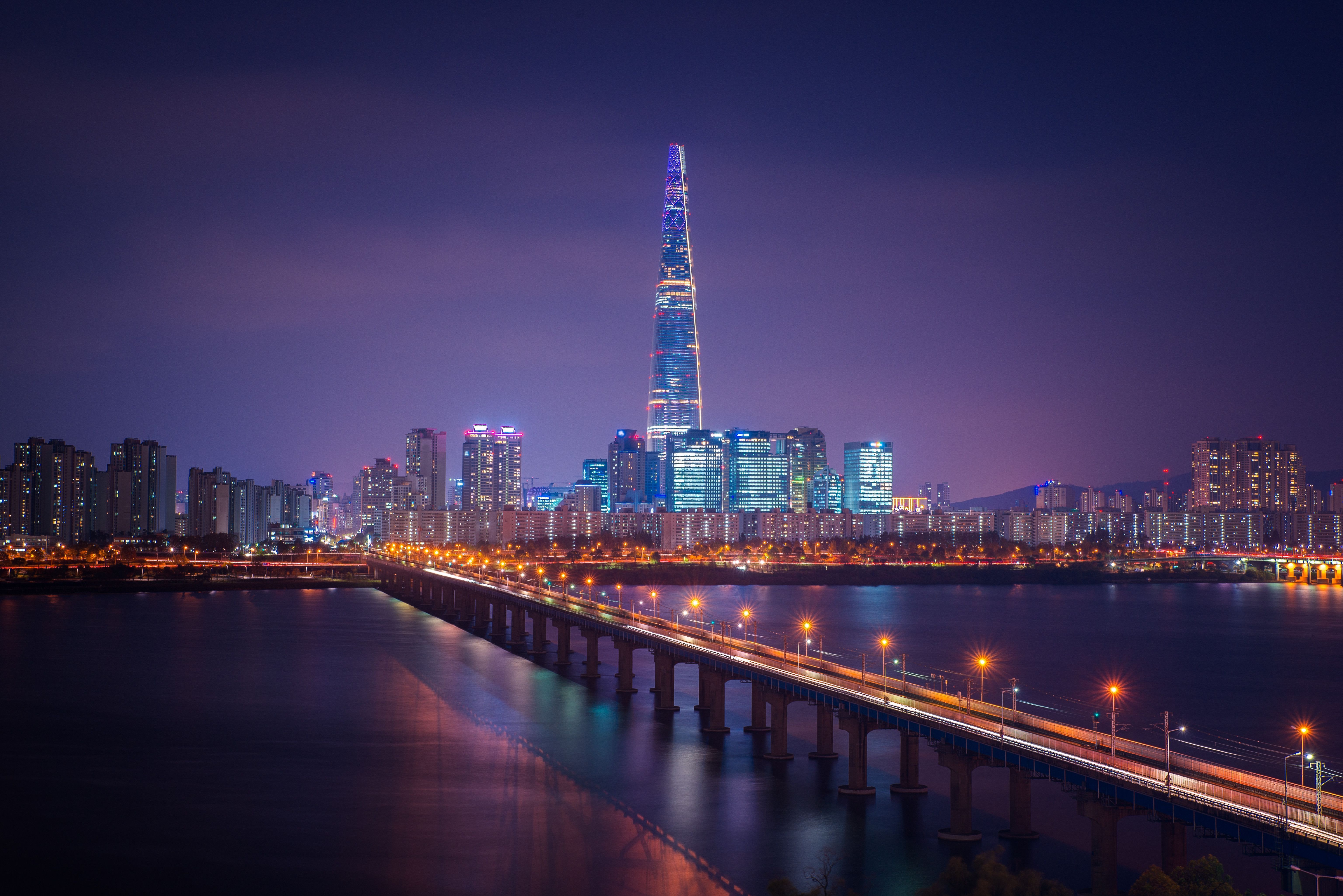 A city skyline at night with a tall building in the center and a river below. - Seoul