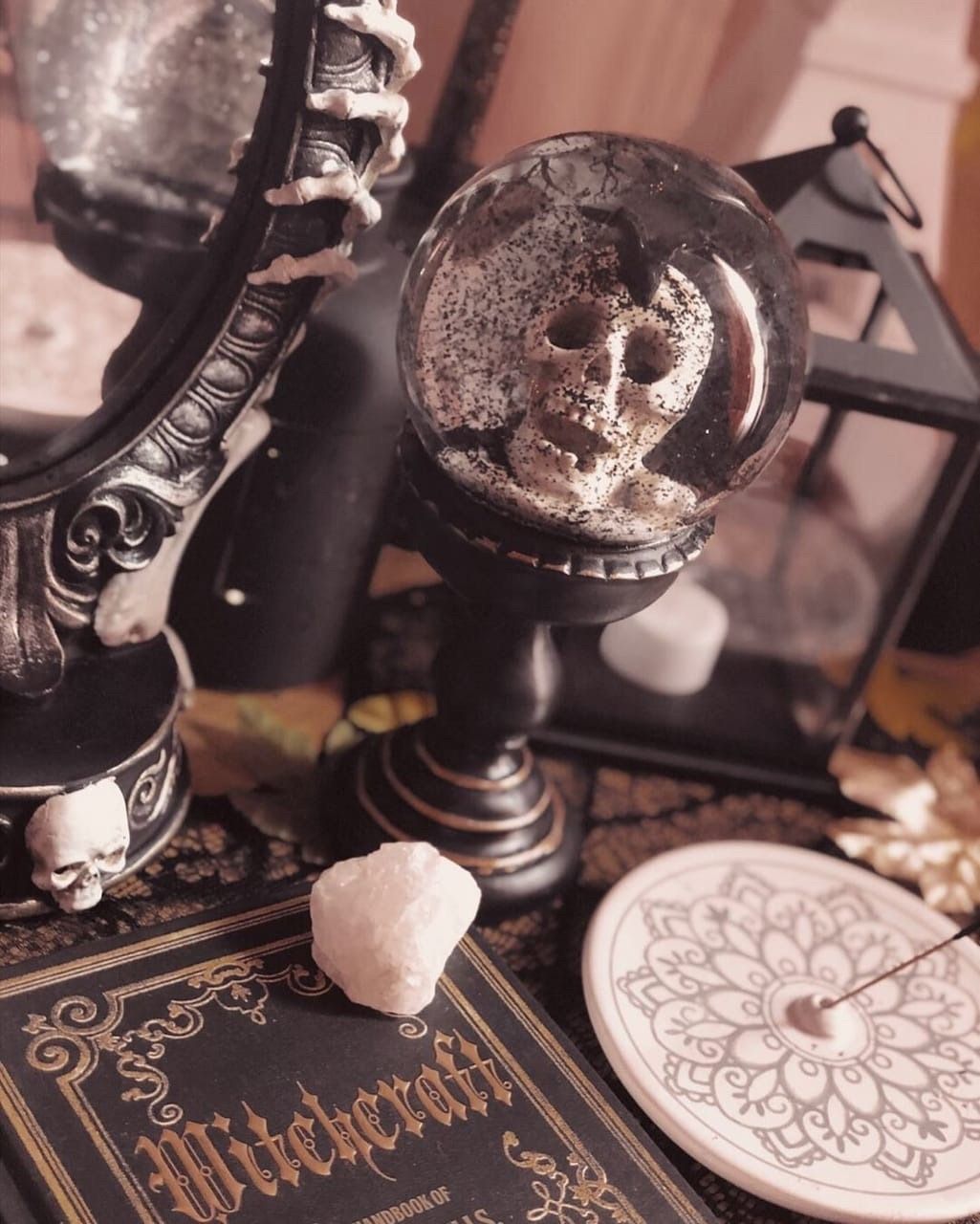 A crystal ball with a skull inside sits on a table with a book and other crystals. - Witchcore