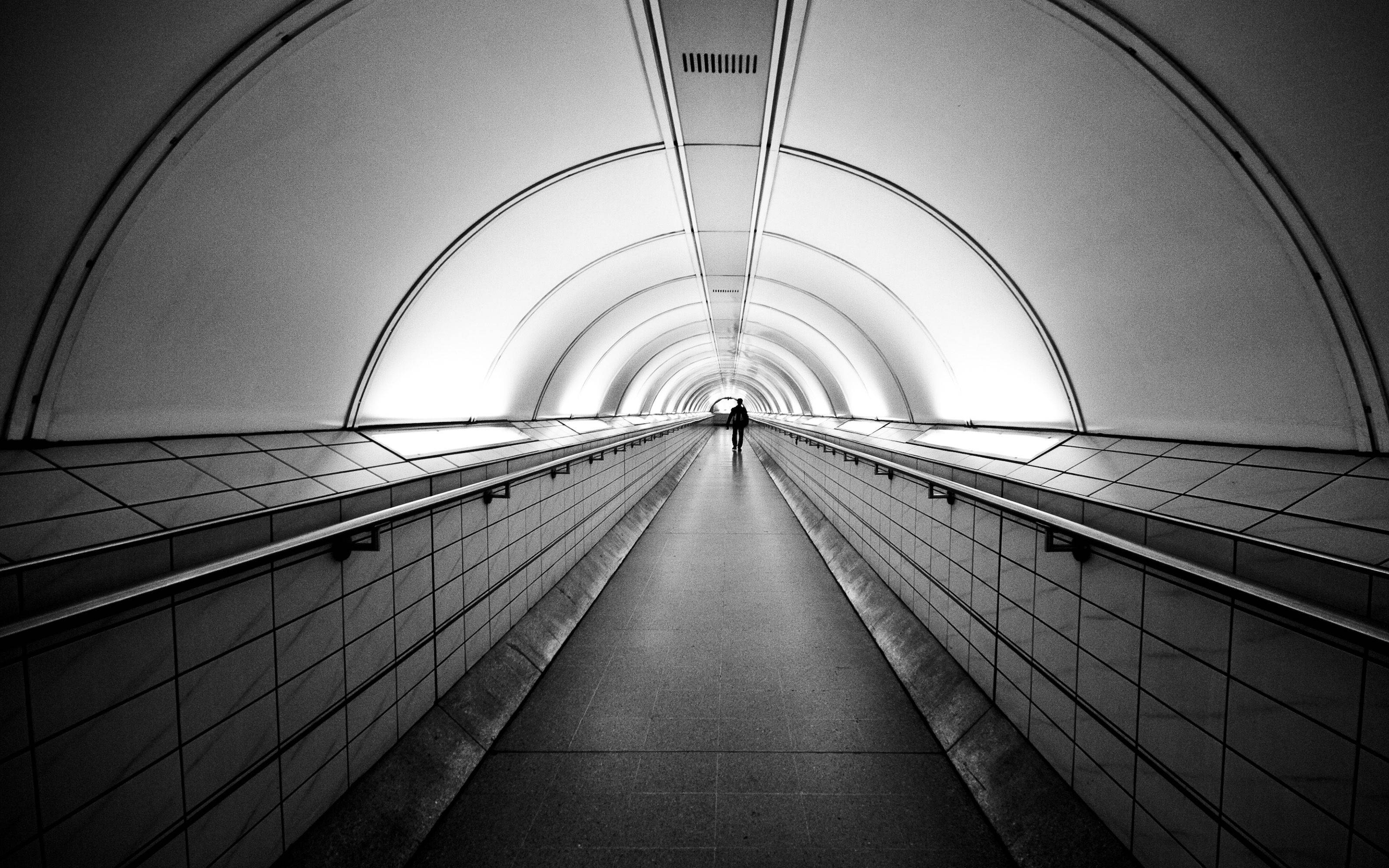 A man walking down a long tunnel. - Gray