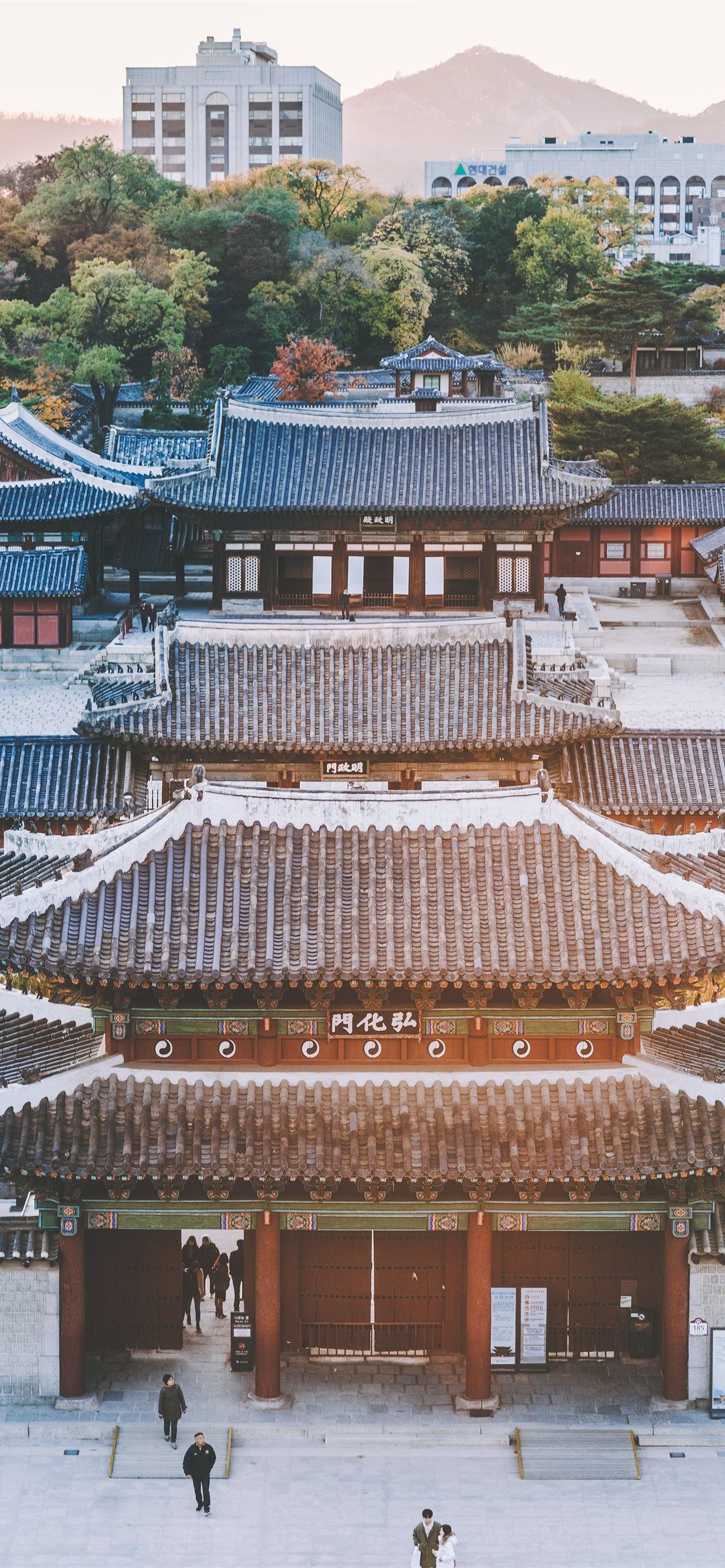 A traditional Korean building with a red roof and people walking around it. - Seoul