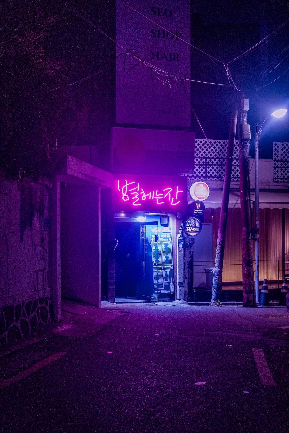 A purple neon sign is lit up in a dark alley. - Seoul