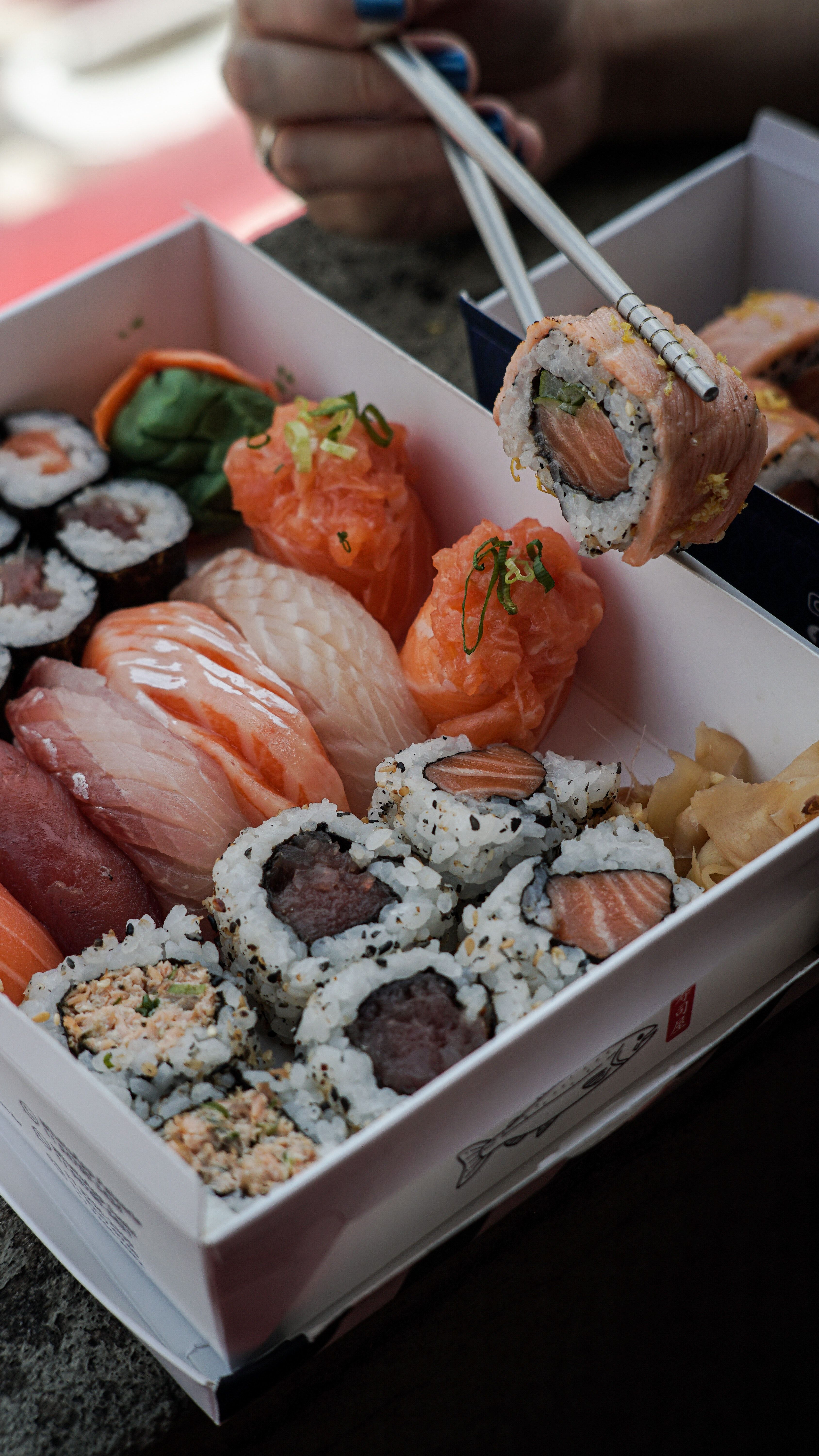 A box of assorted sushi with chopsticks. - Sushi