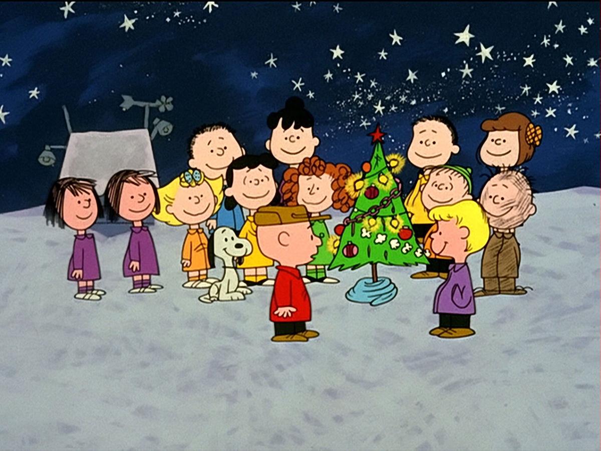 A group of people are standing around the christmas tree - Charlie Brown
