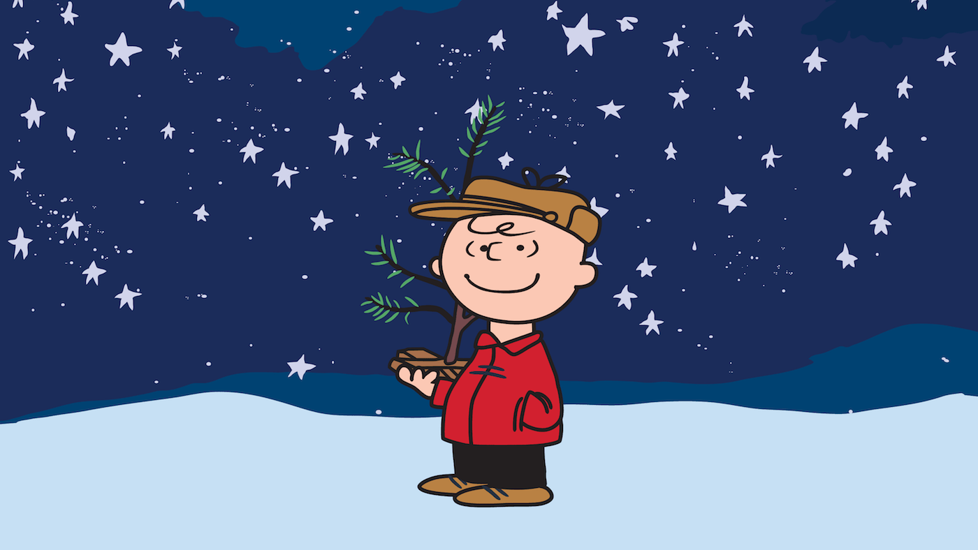 A cartoon character is standing in the snow holding up his christmas tree - Charlie Brown