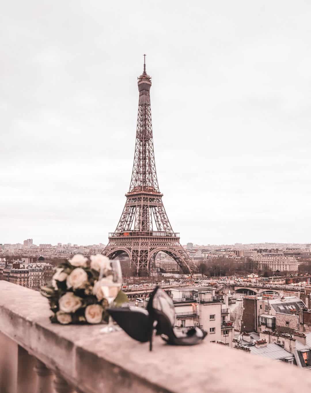 A pair of black high heels and a bouquet of white roses sit on a ledge in front of the Eiffel Tower. - Eiffel Tower