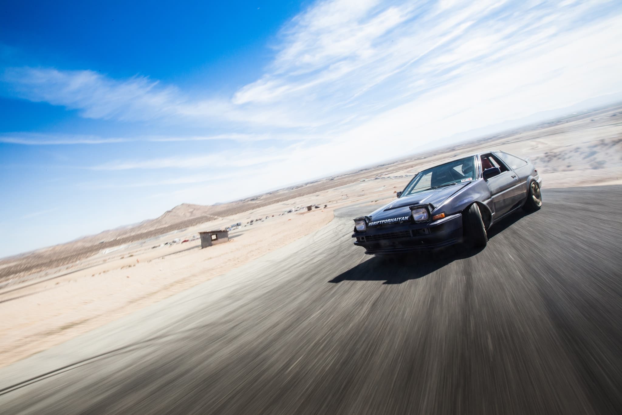 A car is speeding down a road. - Toyota AE86