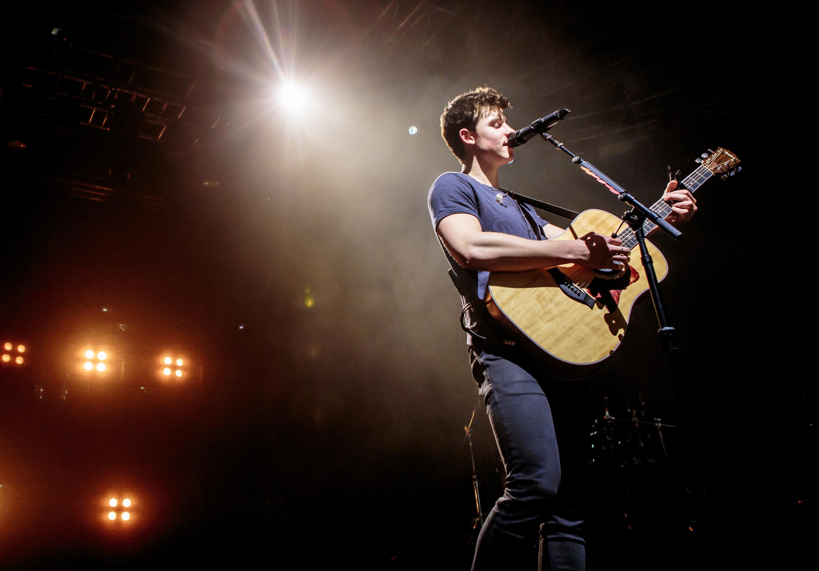 A man playing an acoustic guitar on stage - Shawn Mendes